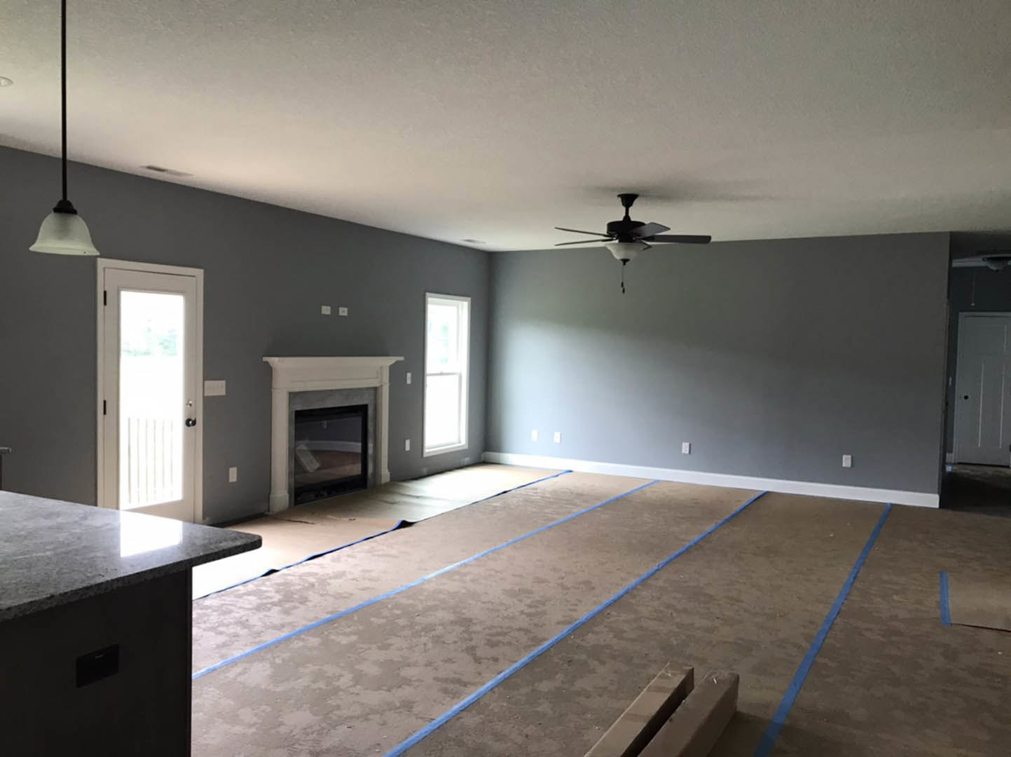 Living room featuring a stone fireplace, ceiling fan with light, white walls, hardwood flooring, glass-paneled door, and large window allowing natural light.