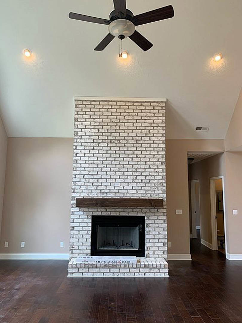 Hardwood floor living room with a black-framed glass fireplace, wood mantel shelf, and ceiling fan with light fixture