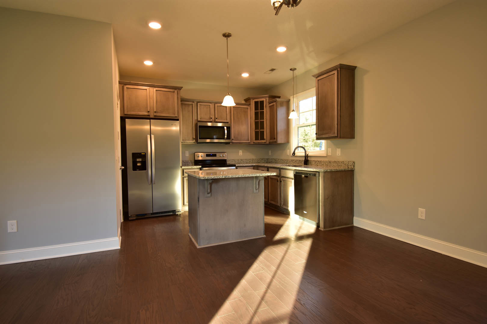 White marble kitchen island with built-in sink, stainless steel refrigerator, wood cabinetry, and large window providing natural light