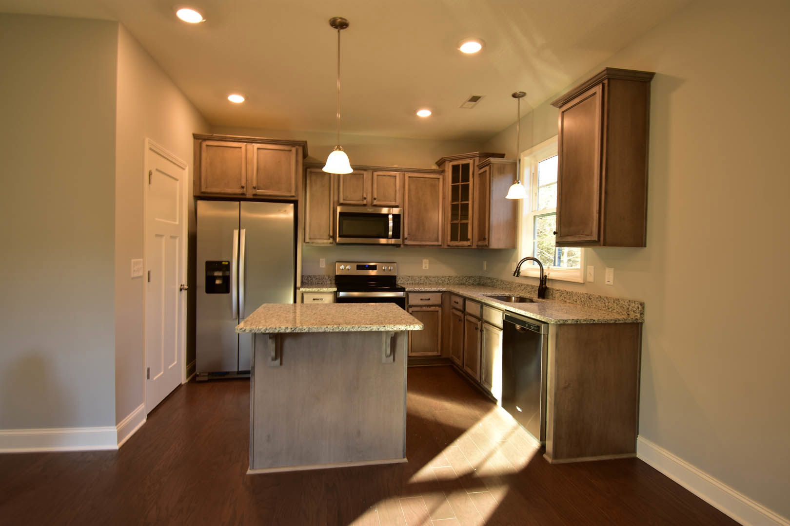 Granite countertop kitchen with stainless steel refrigerator, wooden cabinetry, marble-topped island, built-in microwave, and tile flooring