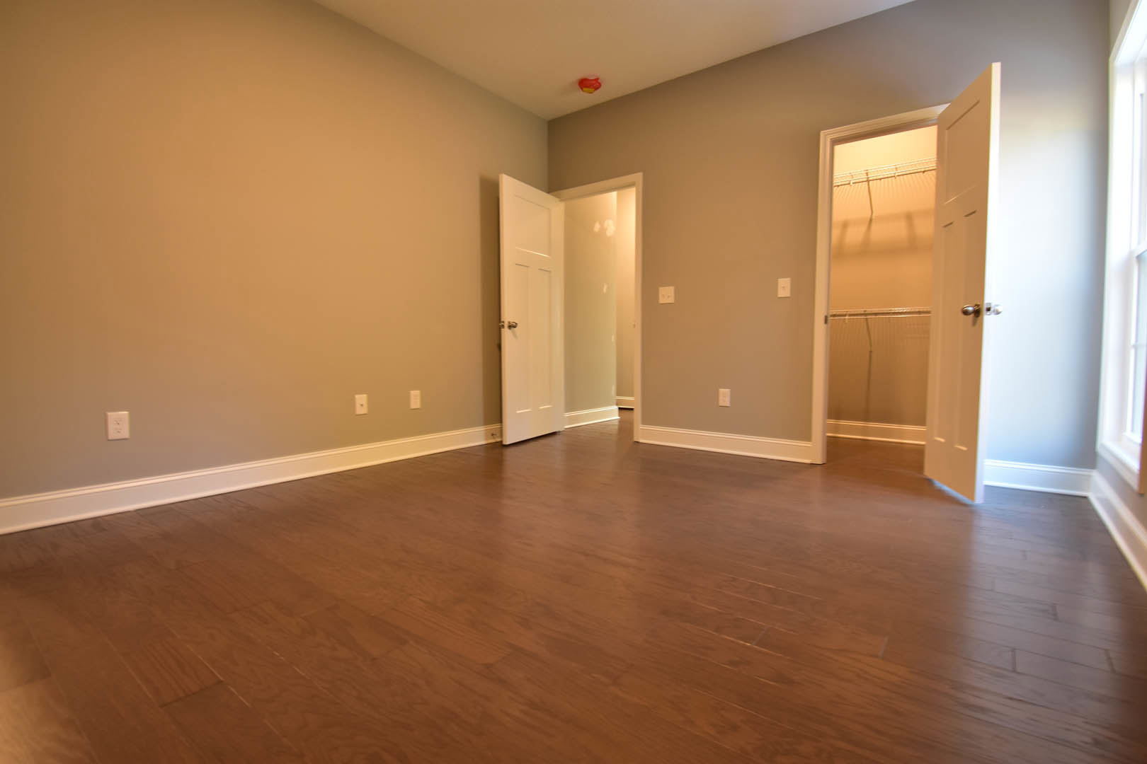 Open doorway leading to a room with hardwood flooring, white walls, and a closet door; light switch visible on the wall.