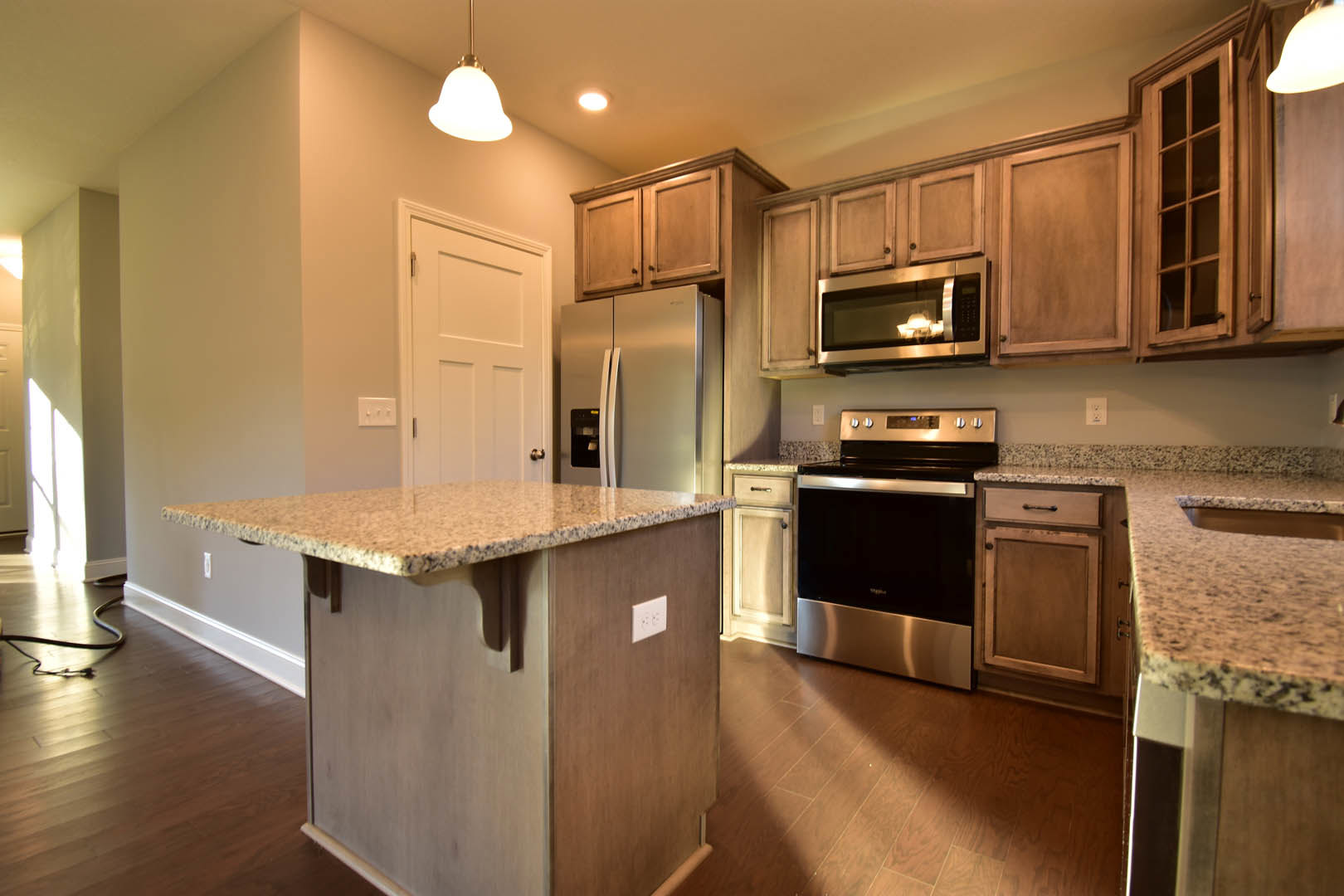 Marble island with waterfall edge, stainless steel oven and microwave, white outlet on brown wall, wood cabinetry, light hardwood flooring