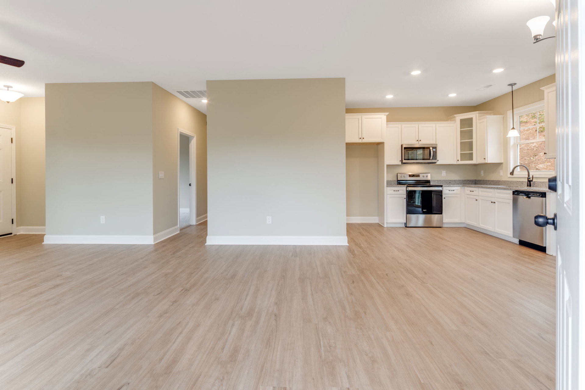 Open kitchen and living room featuring wood flooring, white baseboards, white walls, modern cabinetry, stainless steel oven, and large window.