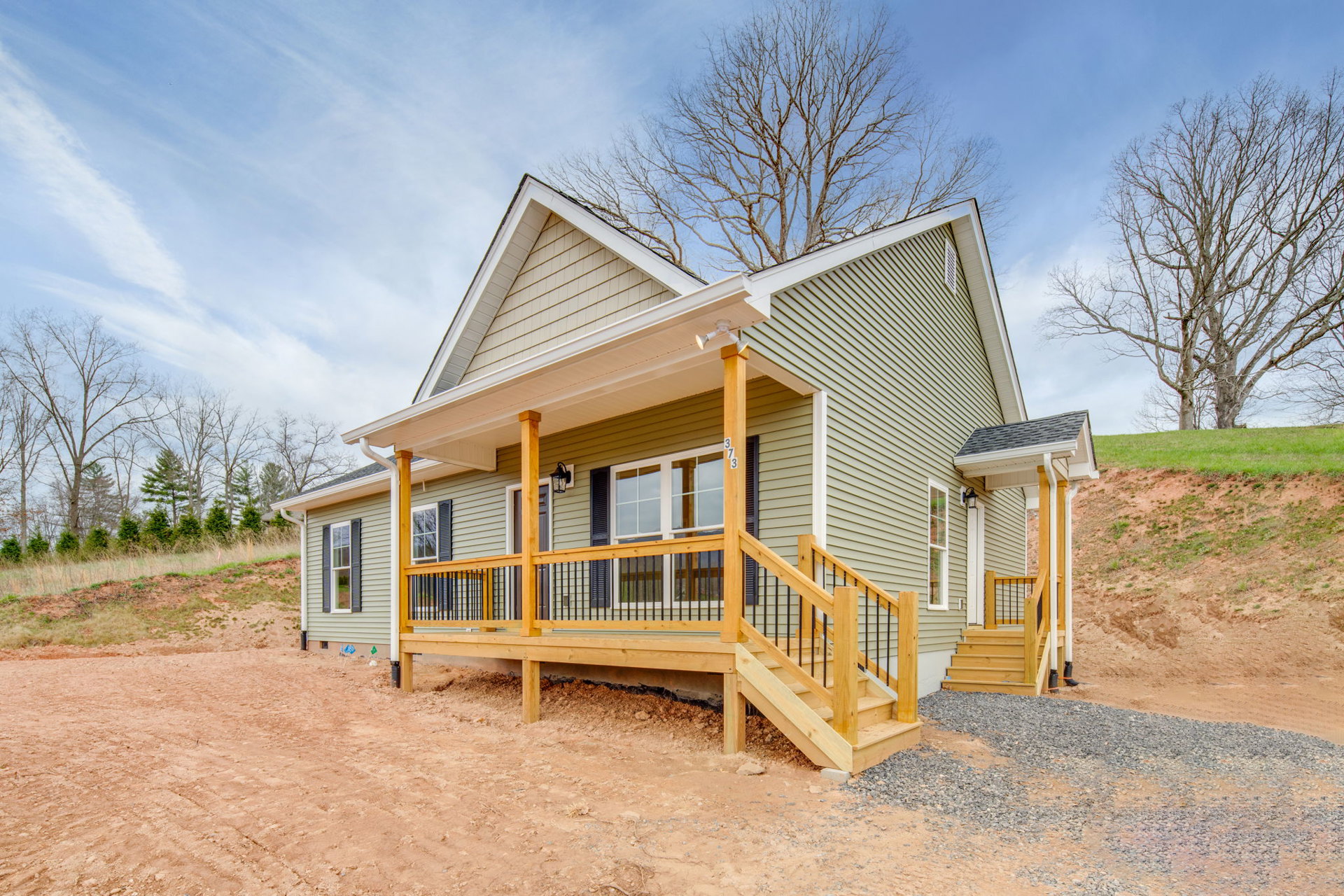 Two-story home with white siding, covered front porch, wooden stairs, railing, leafless tree in yard, cloudy sky overhead