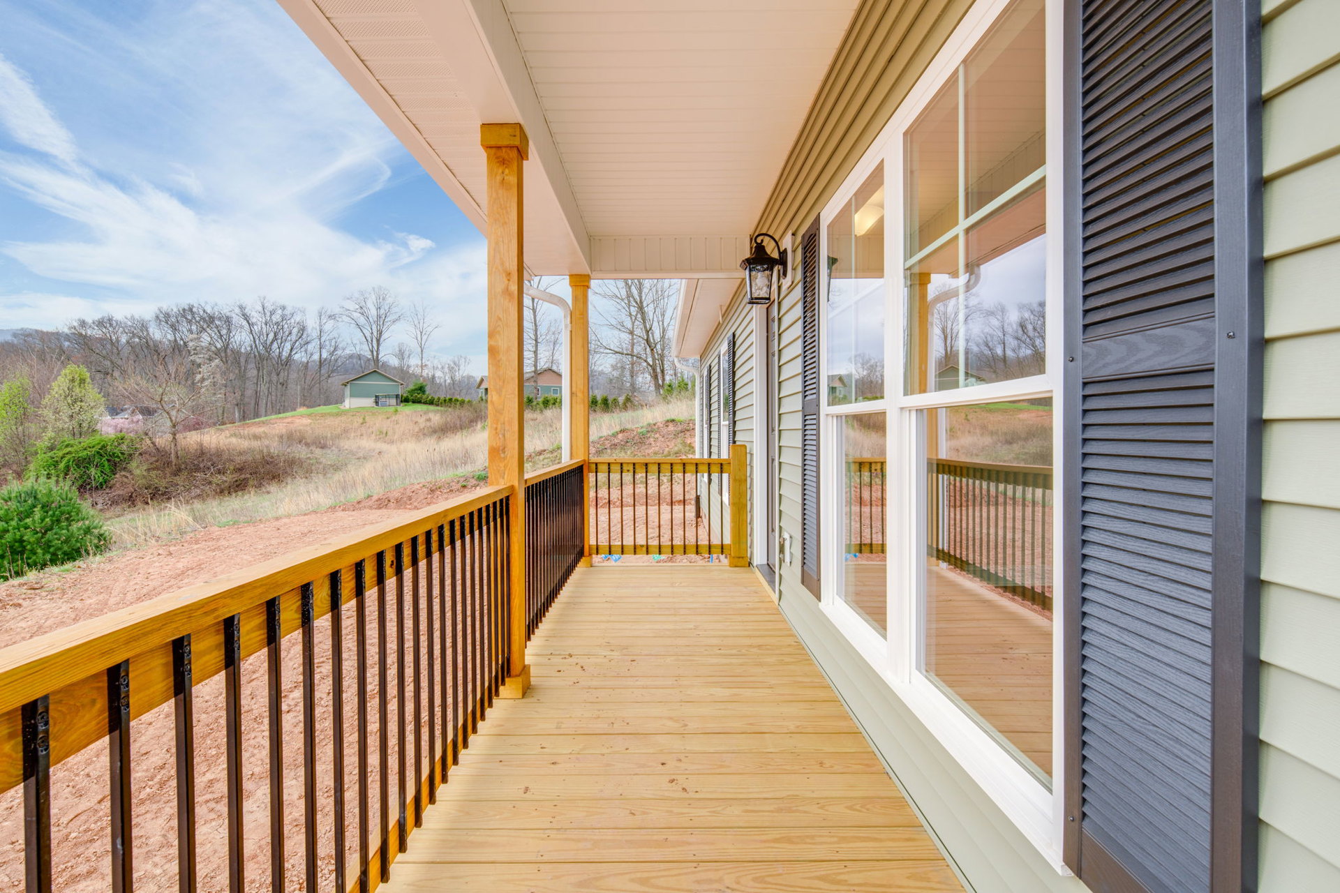 Wooden porch with metal railing, green siding, large windows, and surrounding trees