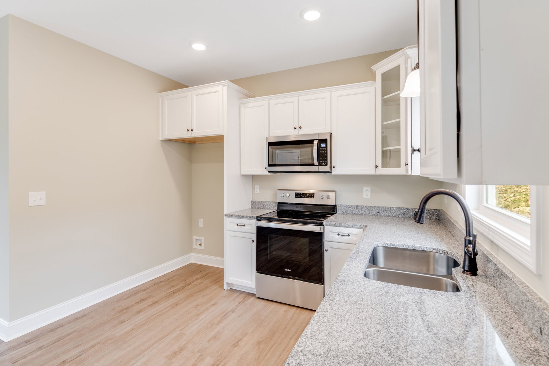 White kitchen cabinets with brushed metal hardware, granite countertops, stainless steel oven and microwave, undermount sink, light switch with two hooks on a tiled backsplash