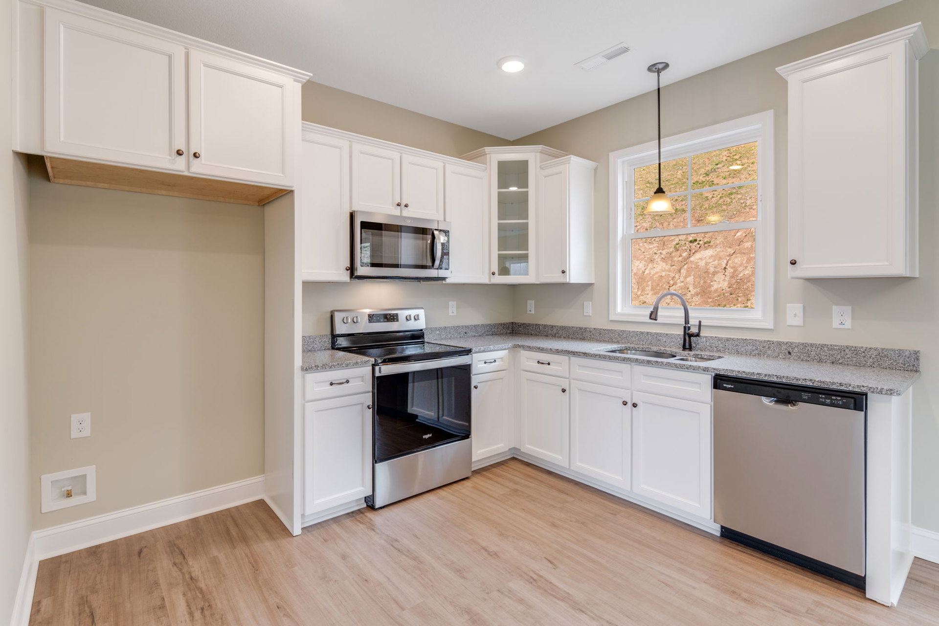 White shaker cabinets, stainless steel oven with glass door, white microwave above stove, quartz countertops, built-in dishwasher with handle, recessed ceiling light, white door