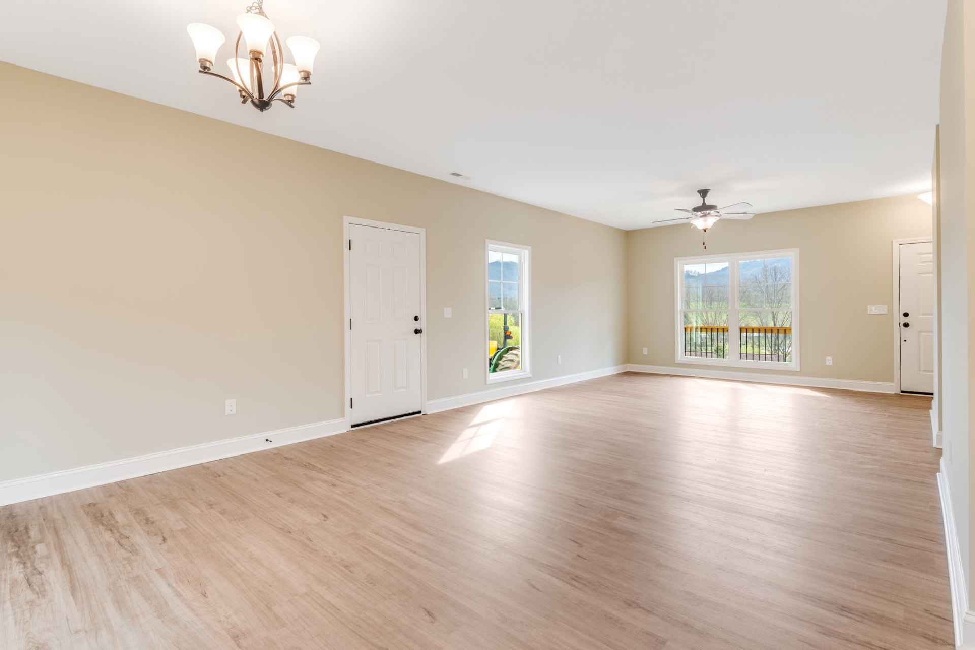 Room with hardwood flooring, white walls, ceiling fan with five lights, white door with black knobs, large window overlooking trees and mountains