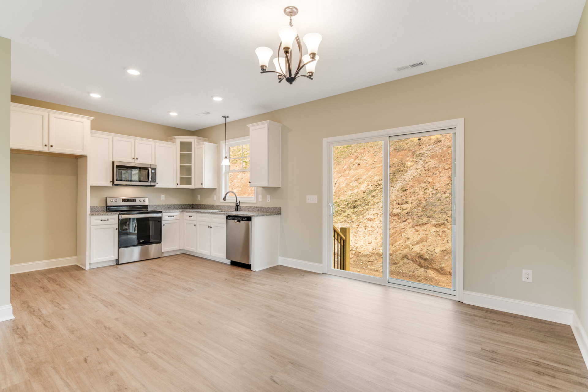 Modern kitchen with hardwood floors, white cabinetry, stainless steel stove and oven, sliding glass door opening to outdoor staircase, five-light ceiling fixture, and open doorway.