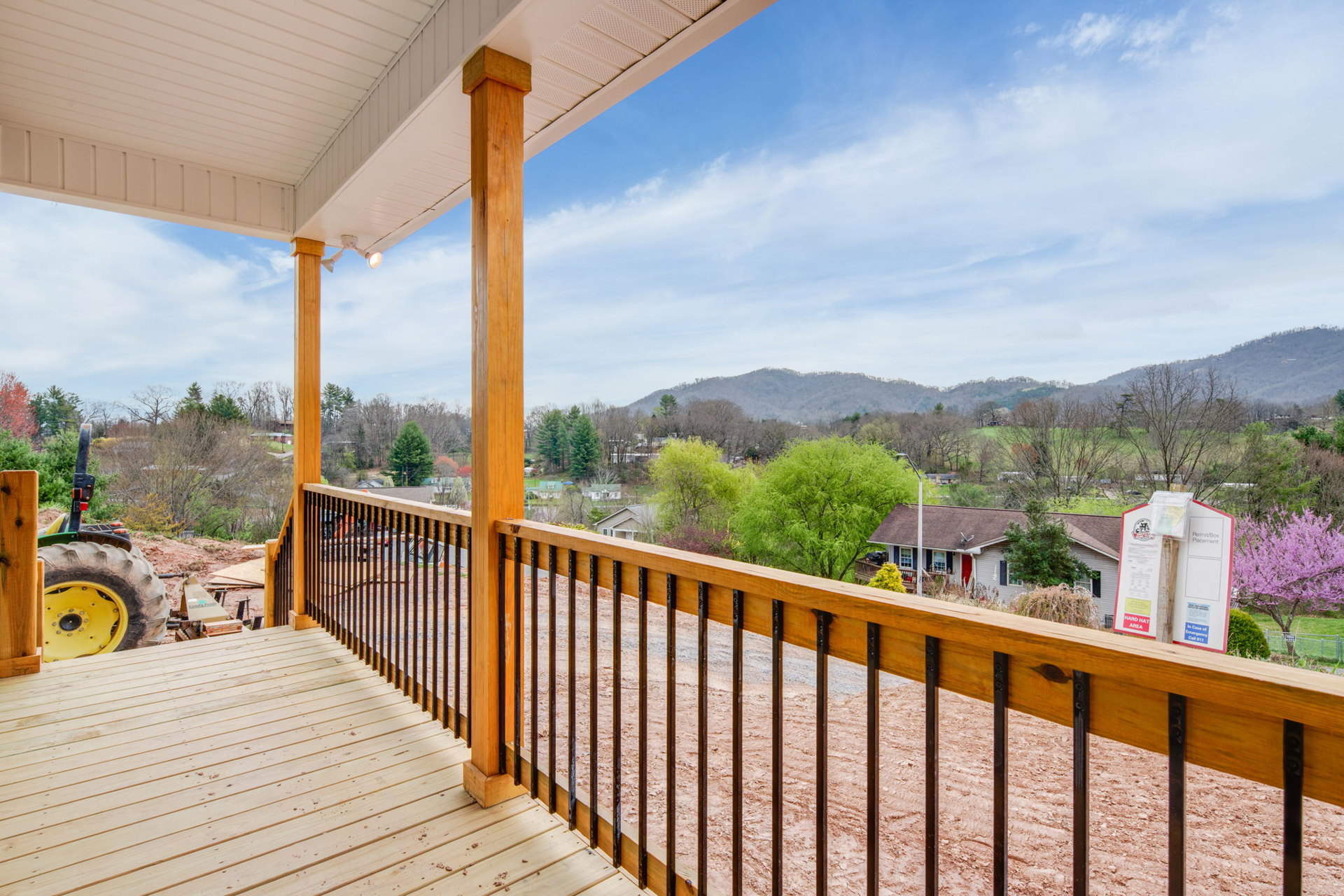 Wooden deck overlooking a town and distant mountains, bordered by a tree with purple flowers, under a blue sky with scattered clouds
