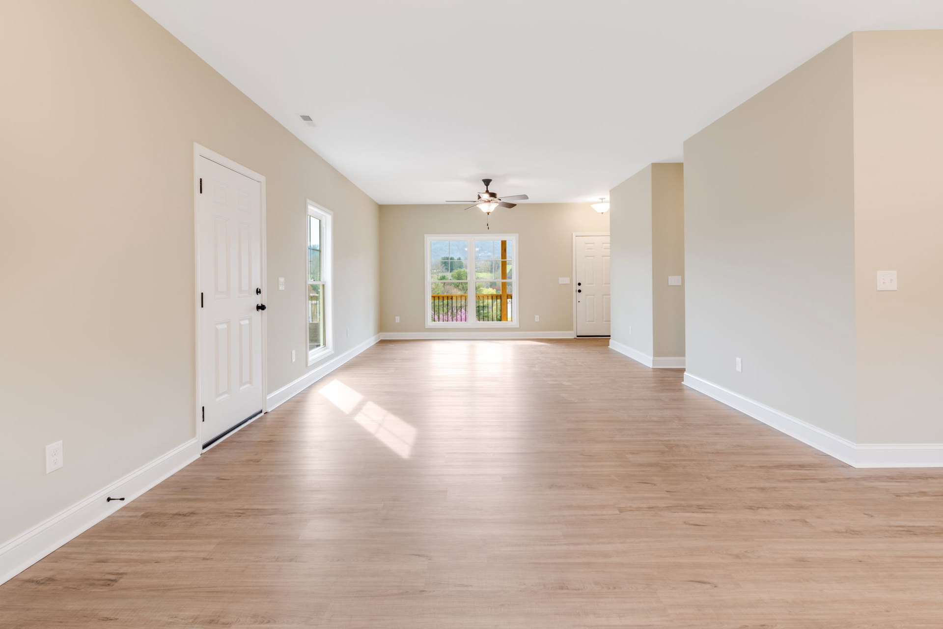 Spacious room with white plaster walls, wood laminate flooring, ceiling fan with light, white door featuring black knobs, and large window with white frame overlooking mountain