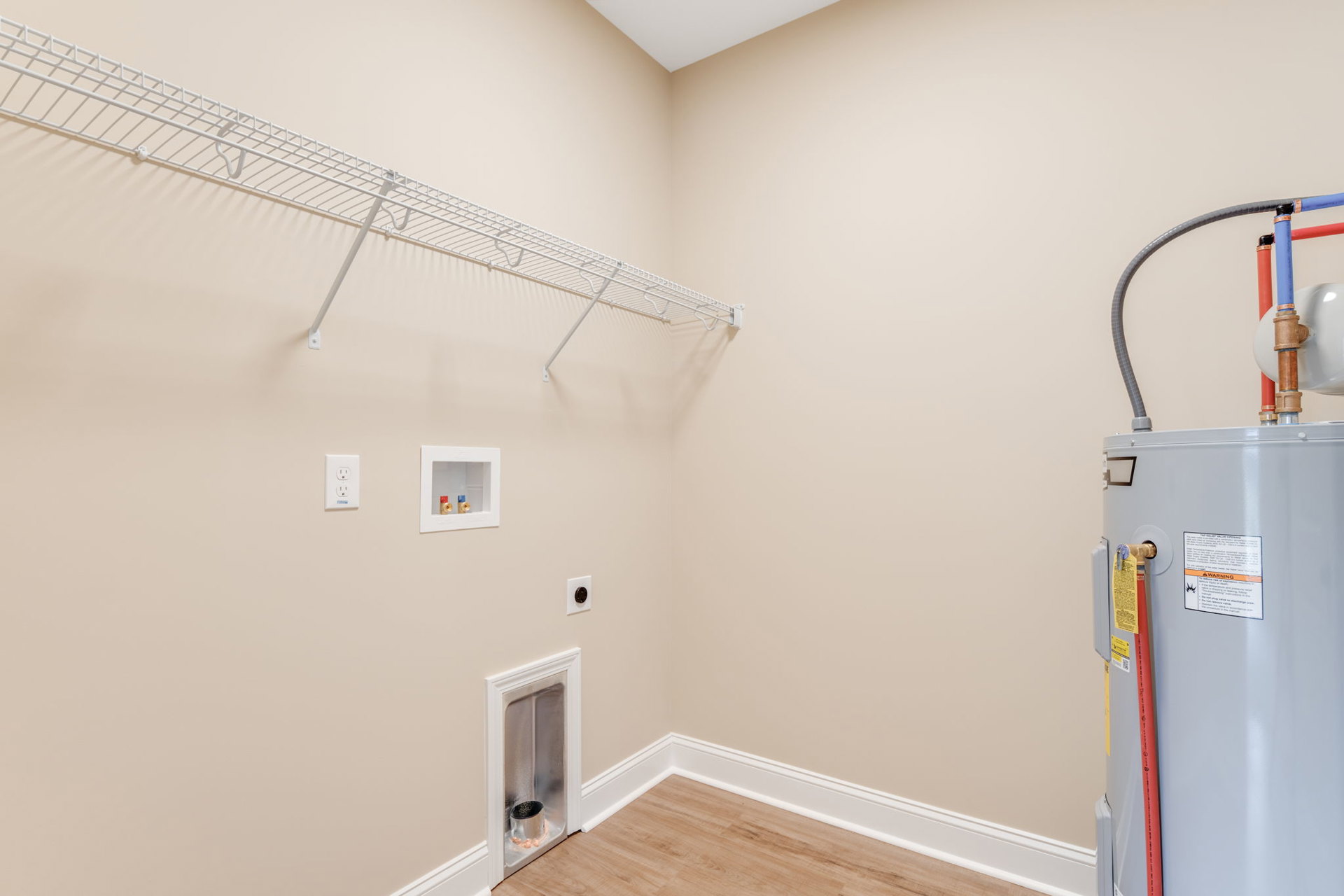 White floating shelf mounted on plaster wall above light wood floor, adjacent to silver water heater and vent, with visible valves and small window on appliance.