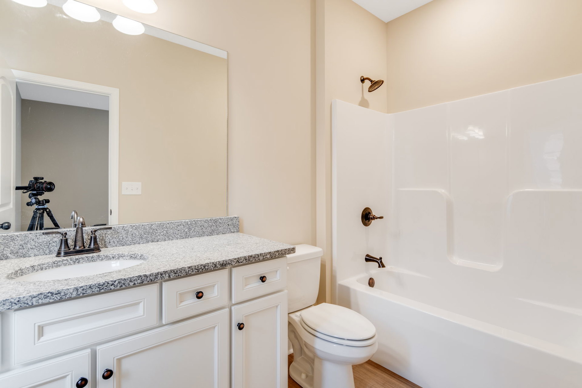 Modern bathroom featuring a freestanding white bathtub, white toilet with closed lid, rectangular sink with chrome faucet, light tile flooring, and white cabinetry with stone