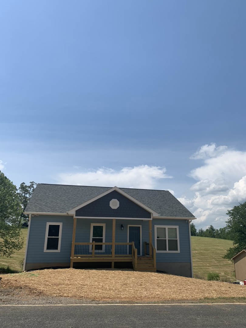 White cottage-style home with covered front porch, wooden fence, gabled roof, white-framed windows, and landscaped yard under partly cloudy sky