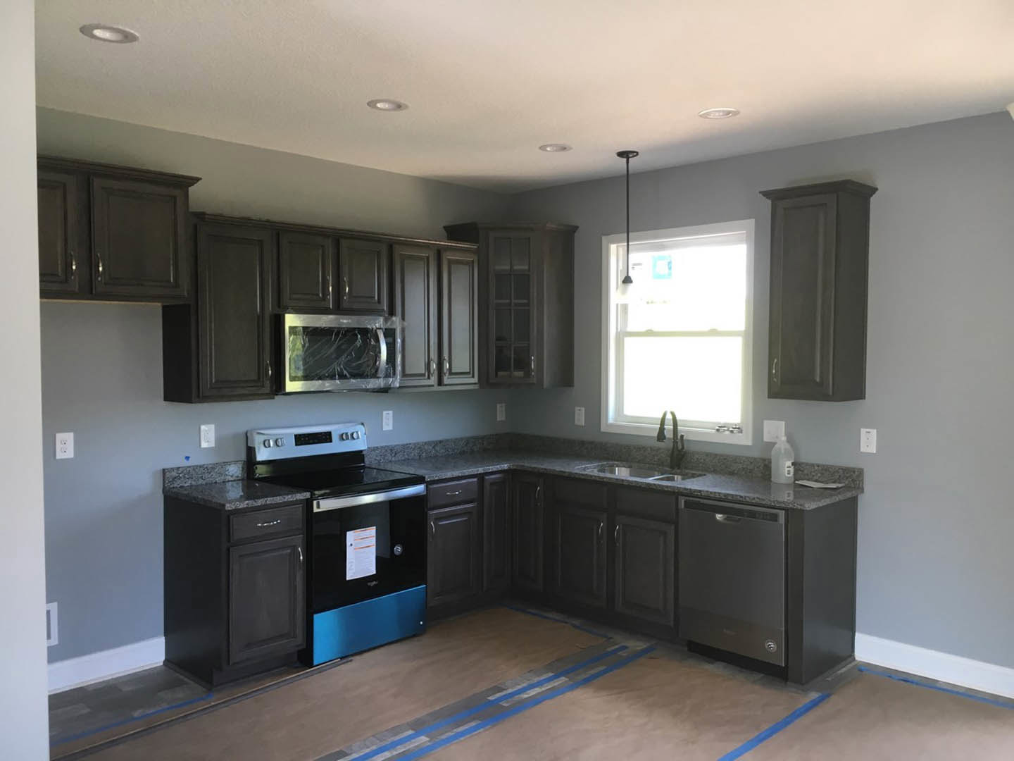 Black kitchen cabinets and matching stove, light streaming through window, microwave with broken screen, white paper with orange and black text on countertop, dark buttons visible