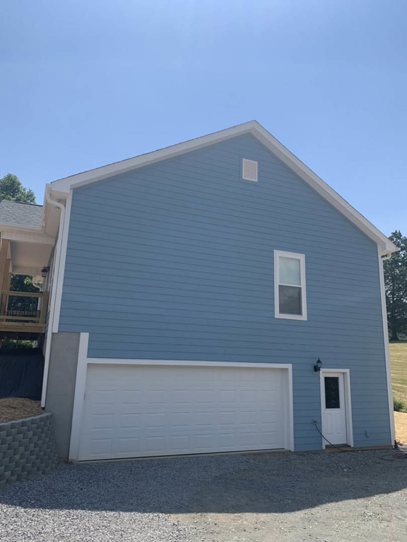 Blue siding exterior with white-framed windows, attached garage featuring a white paneled door, front entry door with glass insert, driveway and landscaping visible.