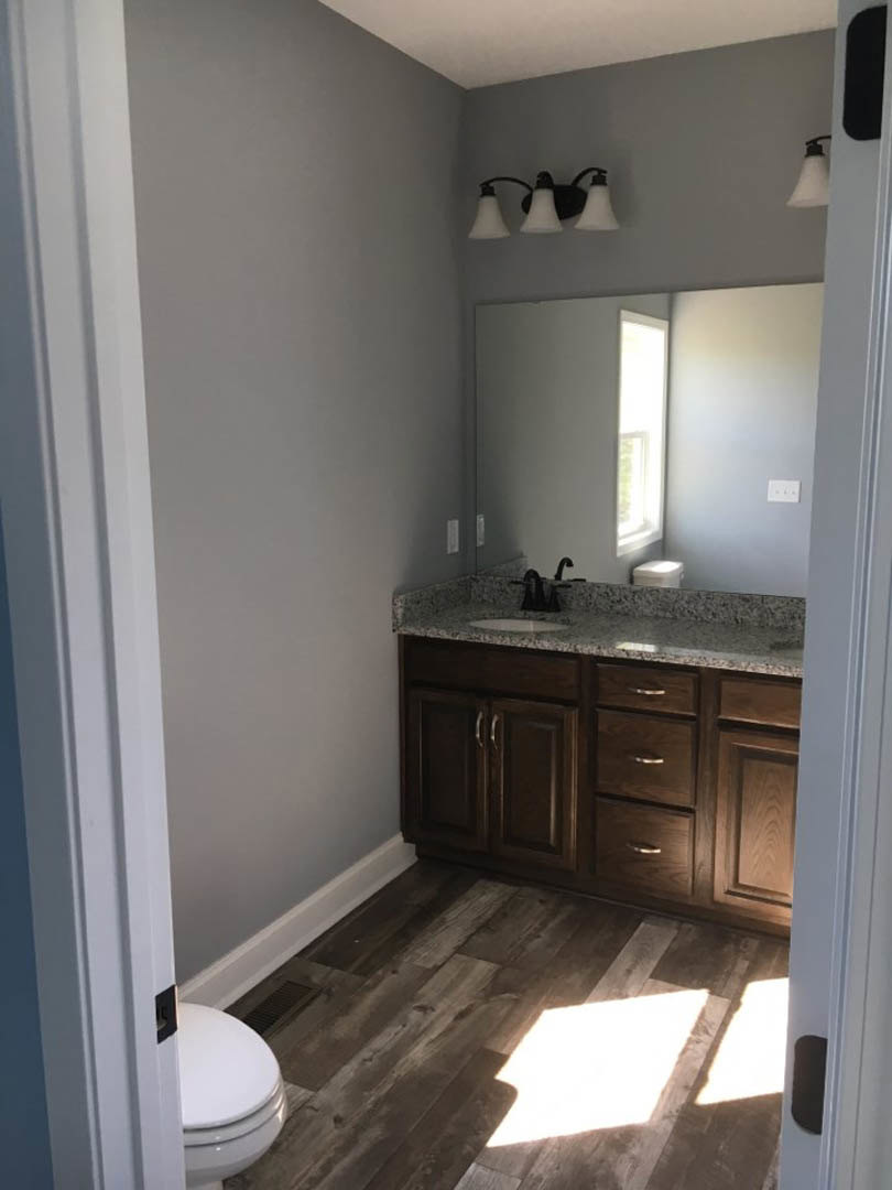 Modern bathroom featuring a white ceramic sink with chrome faucet, rectangular mirror above, light gray tile walls, wood cabinetry, and stone countertop