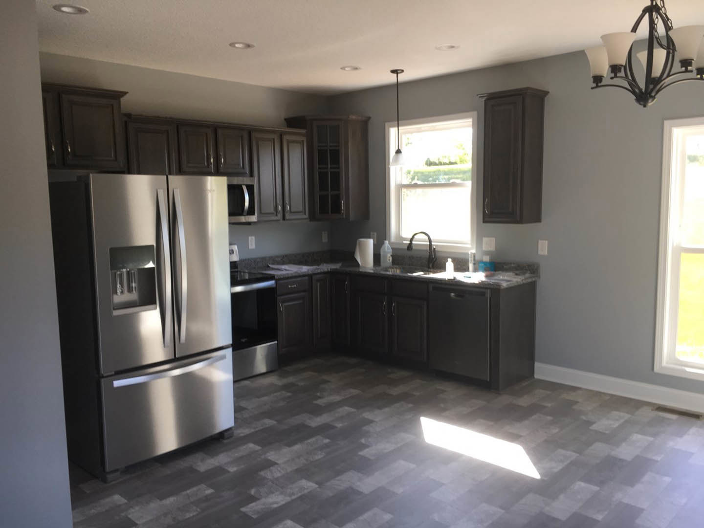 Dark wood kitchen cabinets, stainless steel refrigerator, quartz countertops, modern chandelier, chrome faucet, large window with natural light