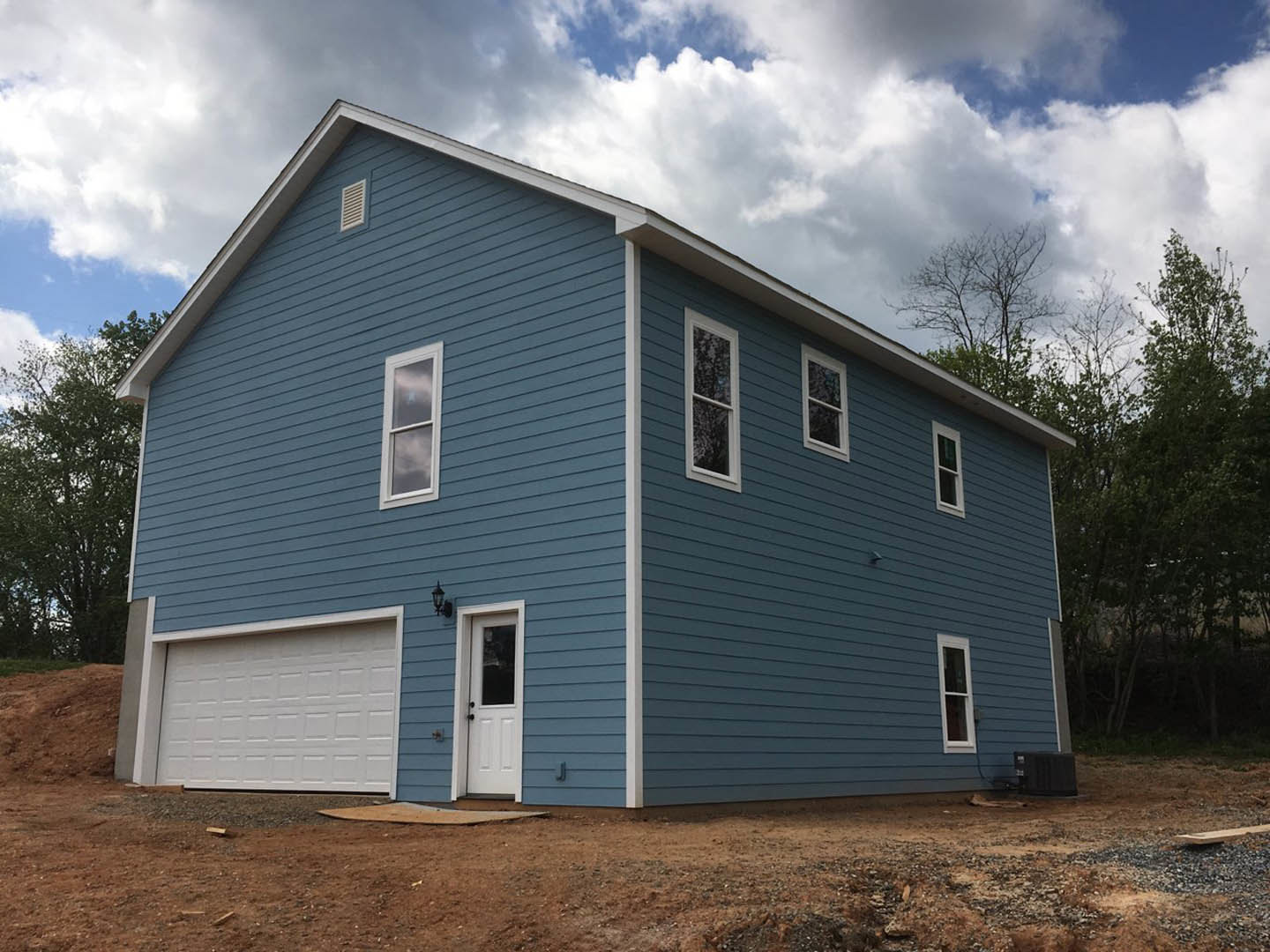 Blue siding house with white trim, attached white garage door, white framed windows, and white entry door with glass panel.