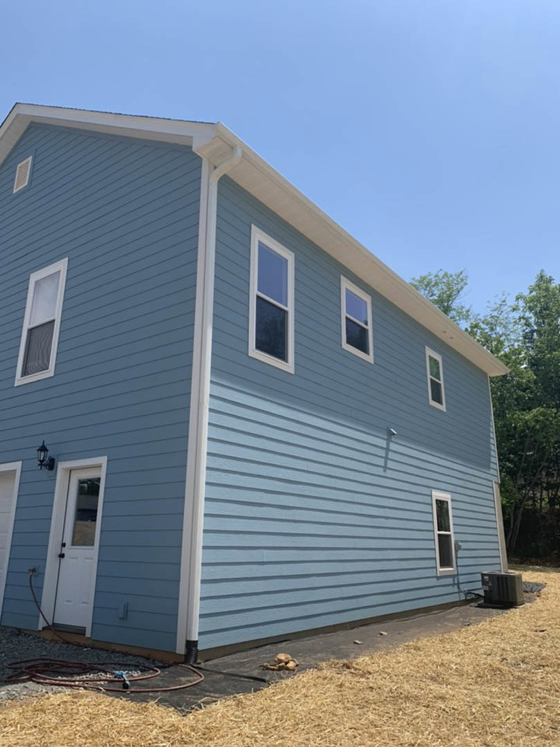 Blue house with white trim, white front door with window, multiple windows, horizontal siding, small tree in front yard, clear sky in background