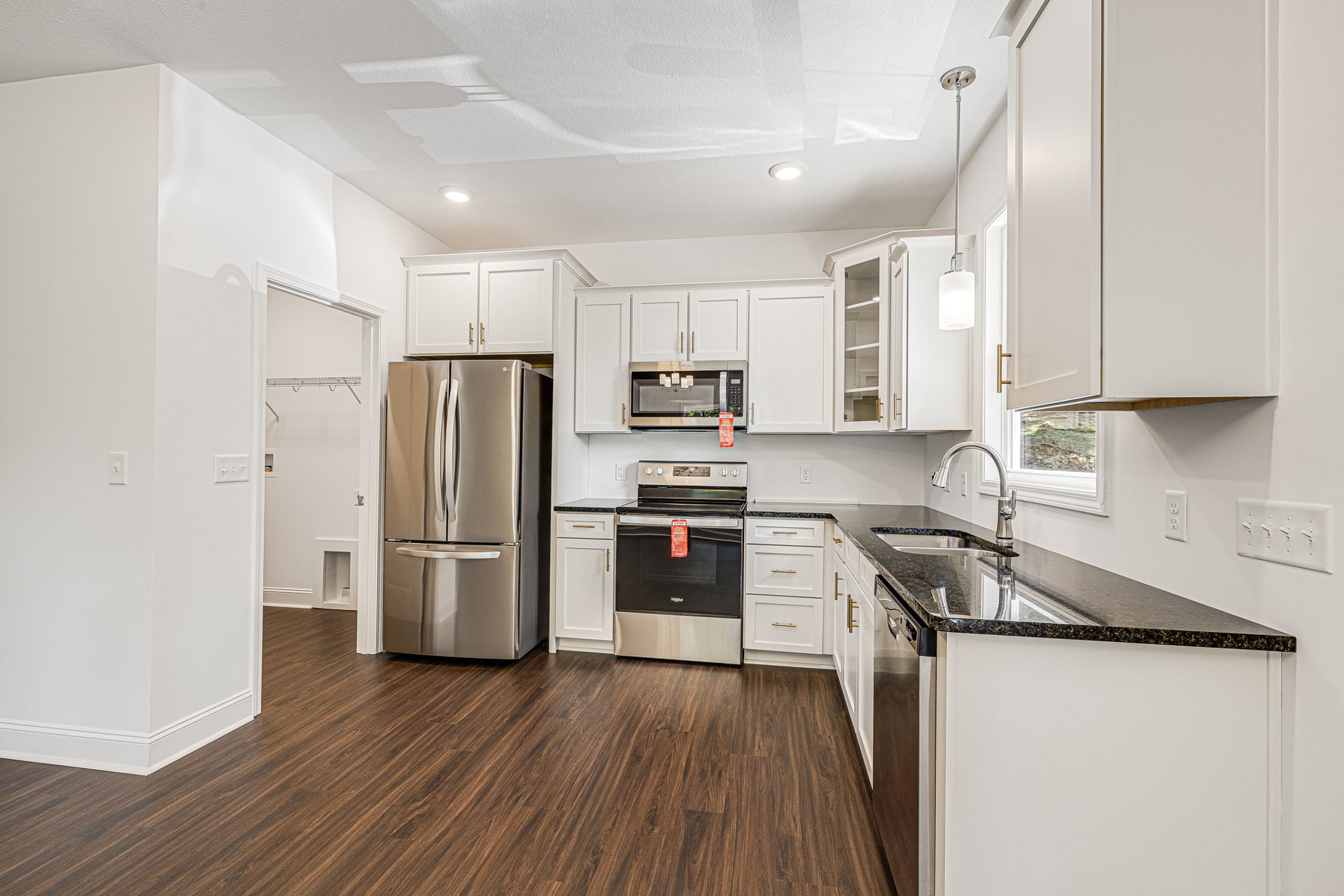 White kitchen cabinets with gold handles, black countertops, stainless steel refrigerator, stove, microwave with light fixture, and wooden flooring
