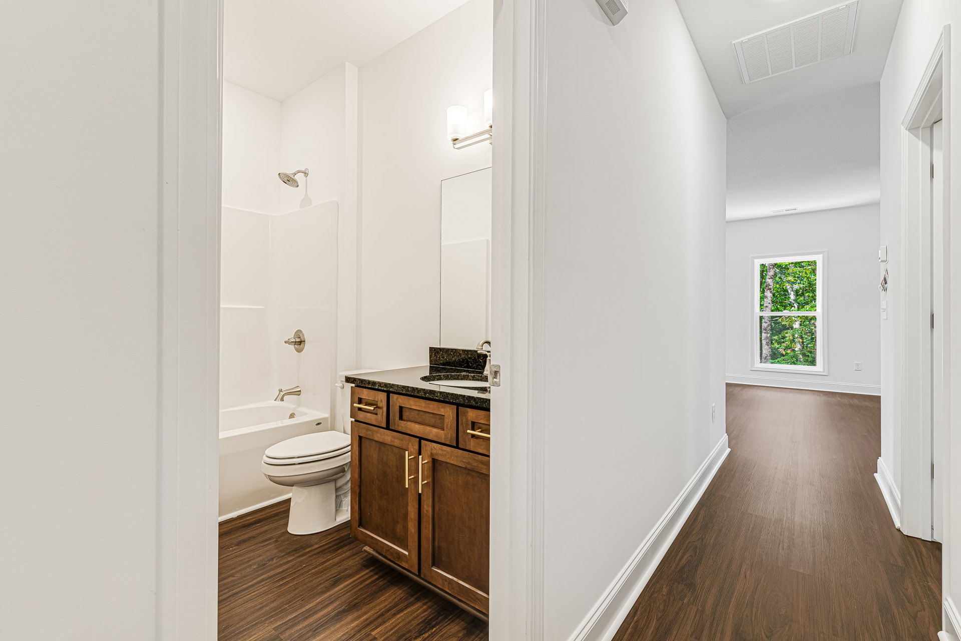 Bathroom with white tile flooring, modern sink and cabinet, toilet with closed seat, window showing trees outside, white ceiling with vent, metal rod light fixture.