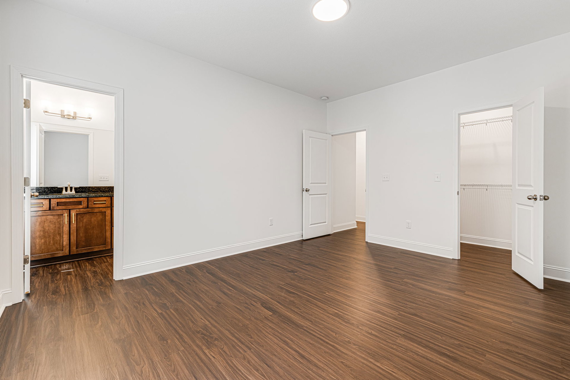 Hardwood flooring, white walls, white door with silver doorknob, white closet, kitchen counter, ceiling light fixture