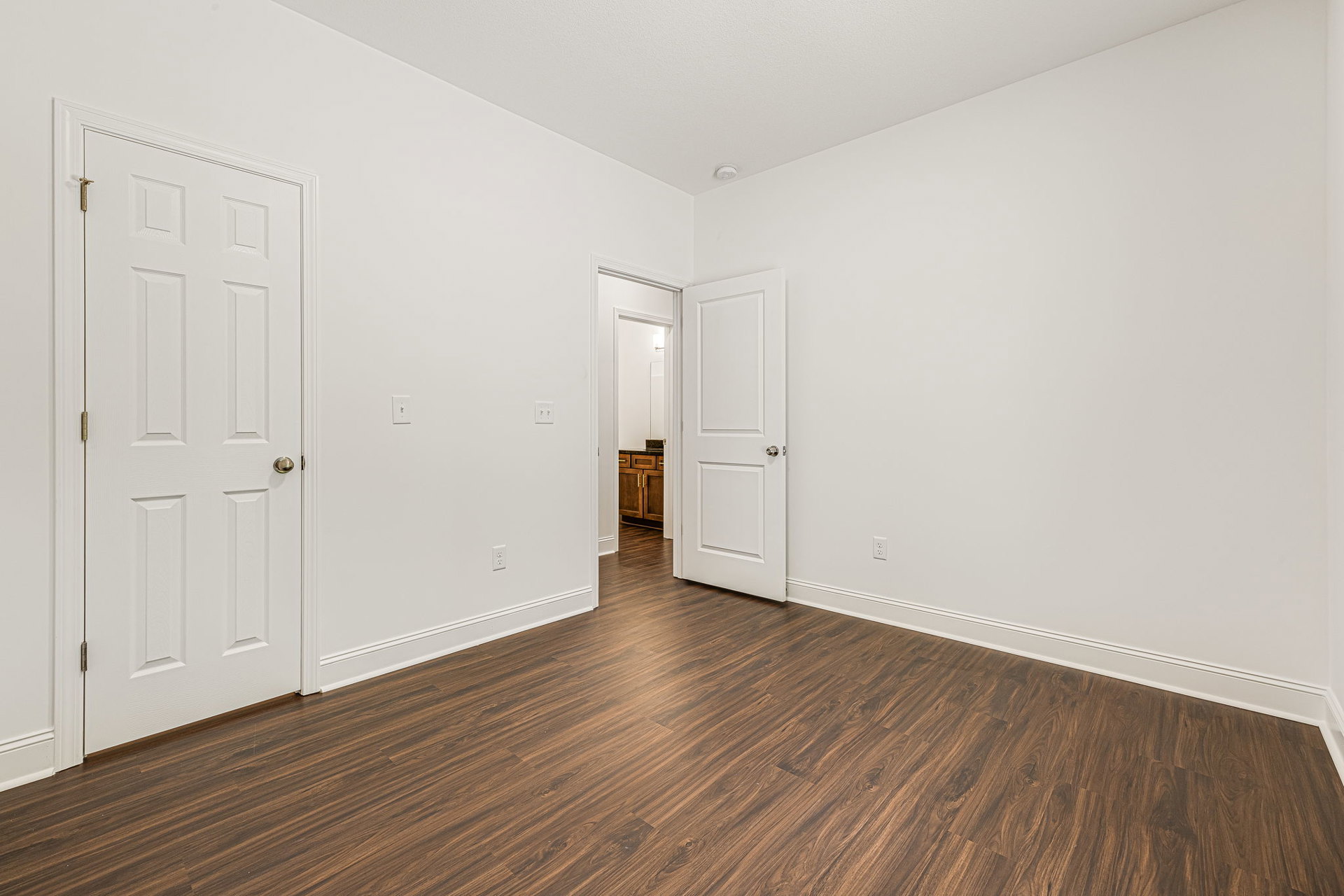 White walls and hardwood floors in a bright room, featuring a white door with a silver knob and a close-up of a white cabinet