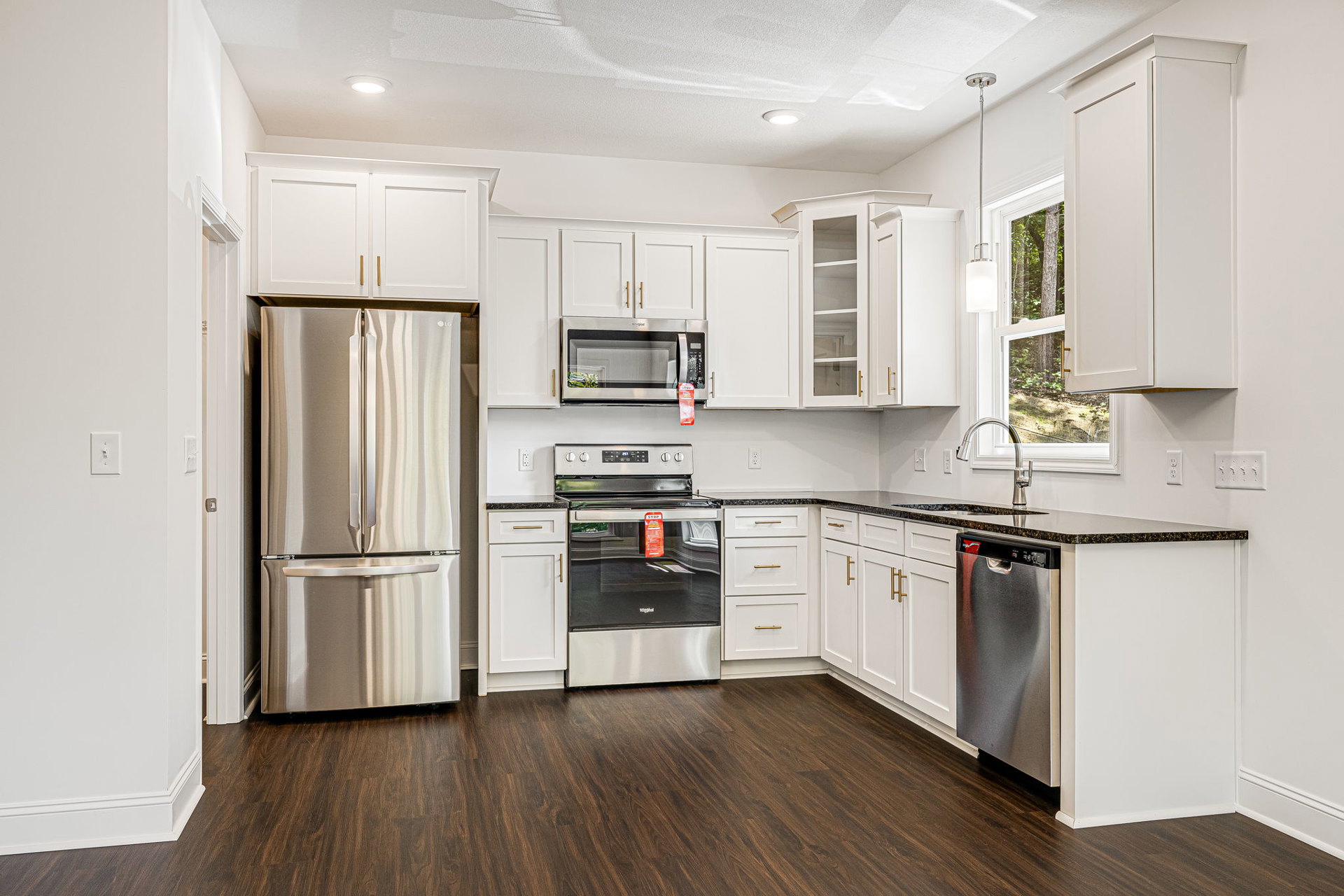 White shaker cabinets, stainless steel refrigerator, stove, and microwave, quartz countertops, hardwood flooring