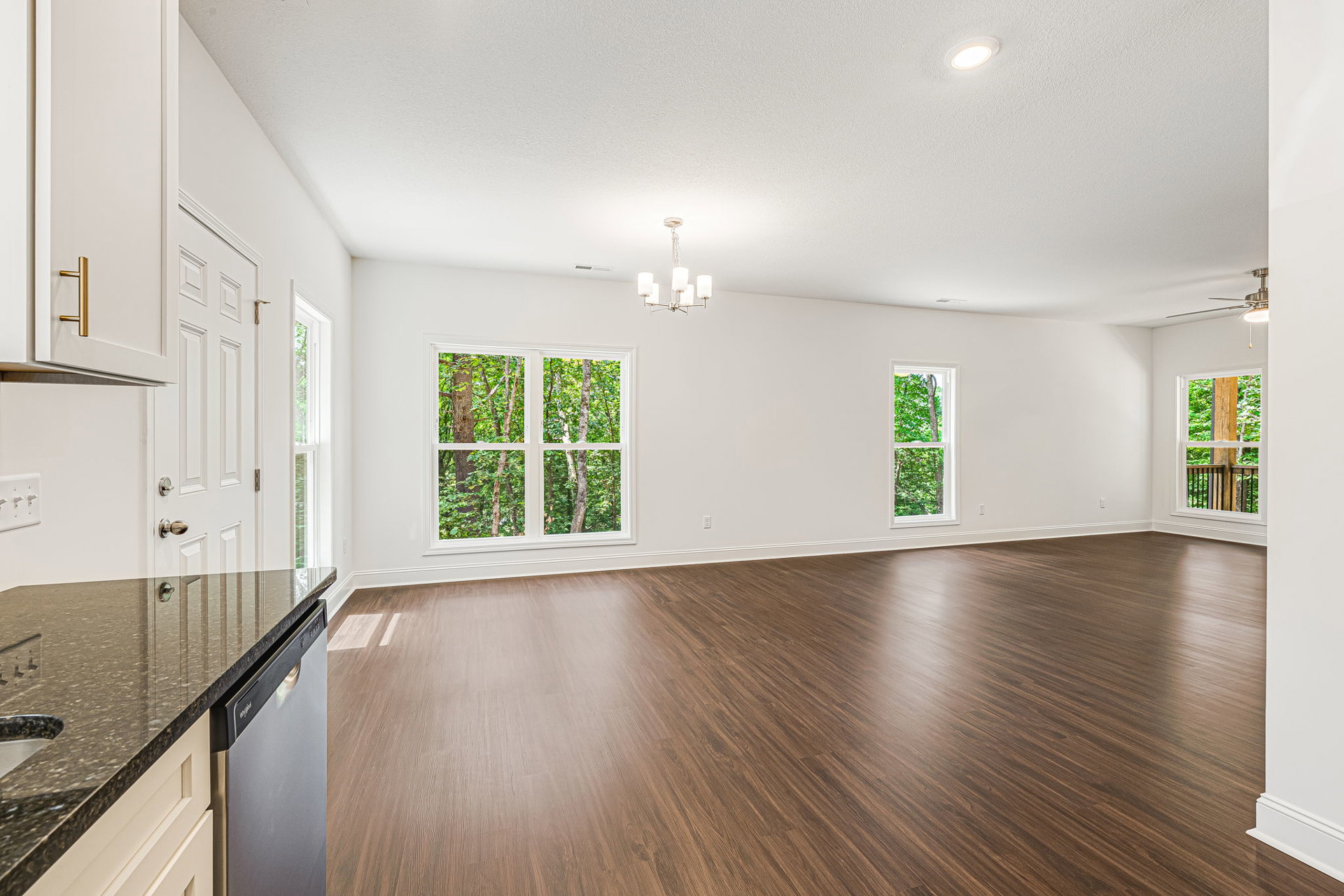 Hardwood floor kitchen with black refrigerator, white chandelier, ceiling light, wood cabinetry, dishwasher, and window overlooking trees