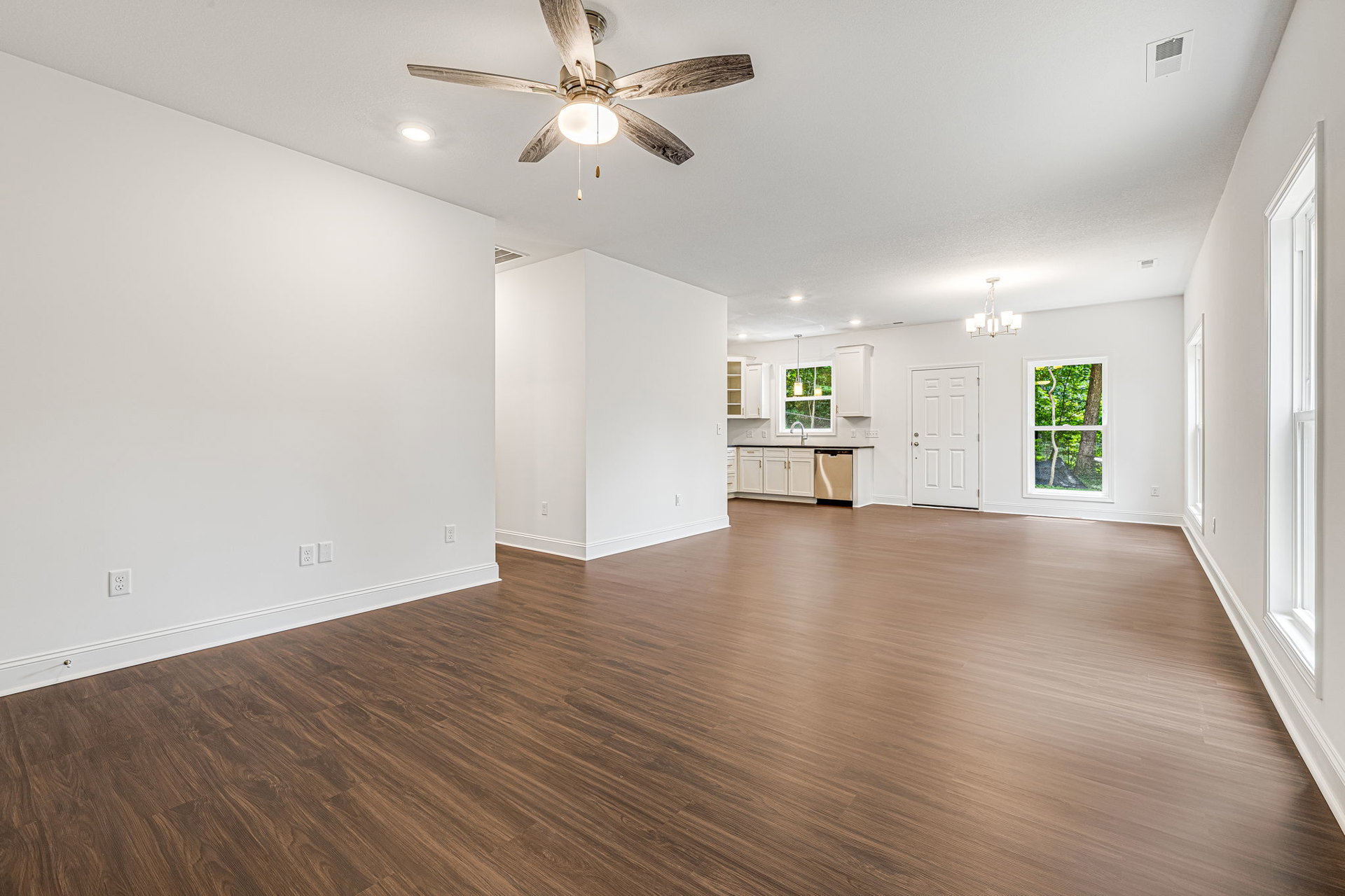 Spacious room with wood laminate flooring, white walls, ceiling fan with light, white-framed window, ceiling vent, and white door with gold handle