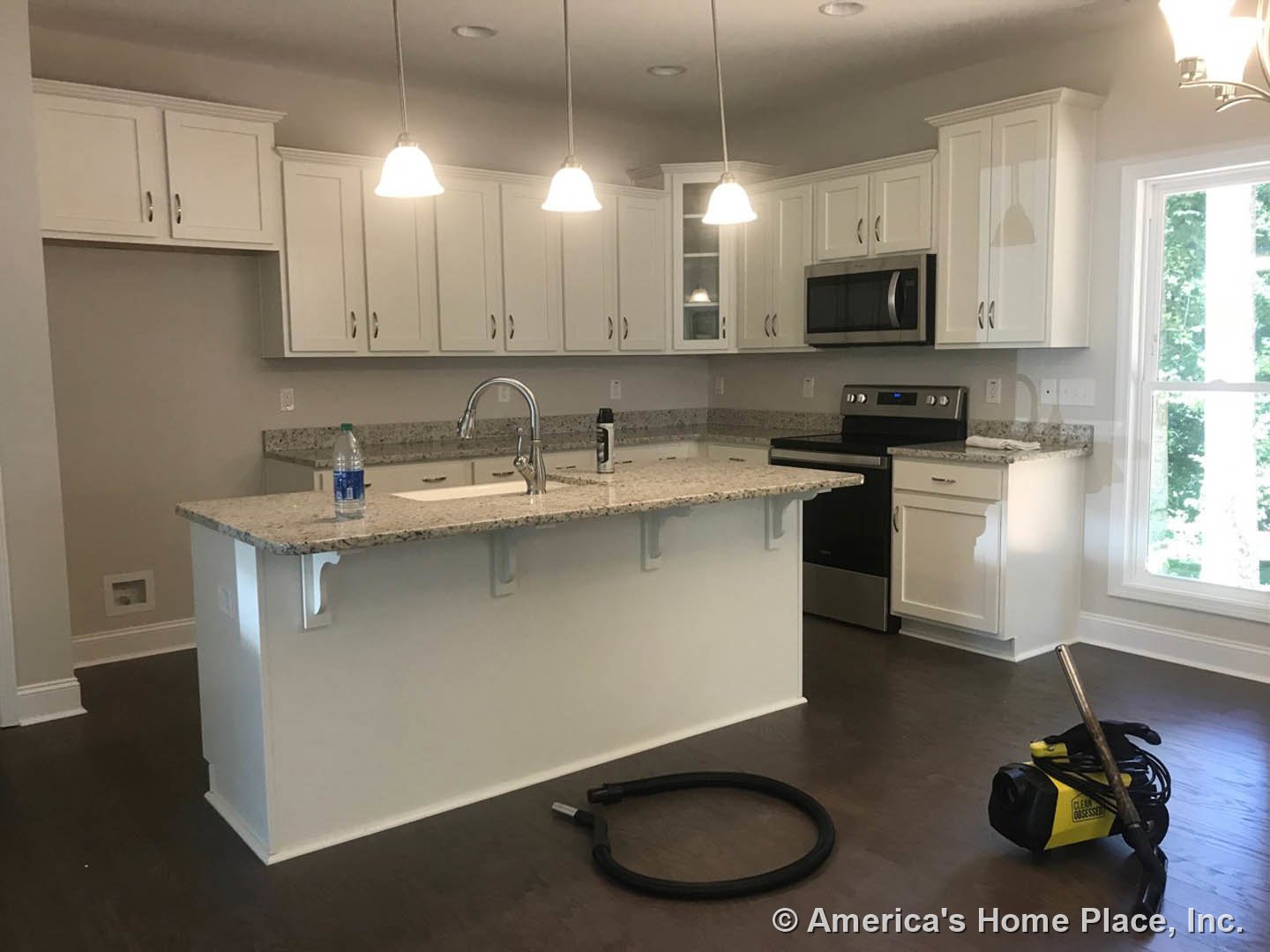 Spacious kitchen featuring a large wood island, yellow and black vacuum cleaner, silver-handled microwave, black rubber ring on countertop, stainless steel faucet, white cabinetry