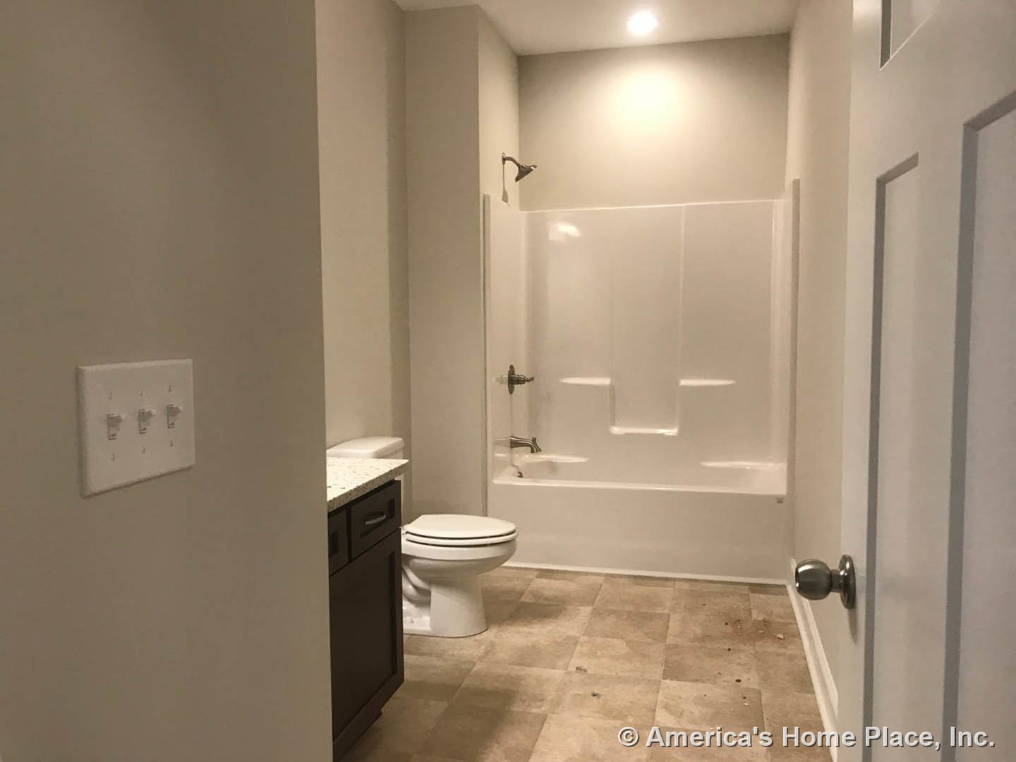 White tile bathroom with a closed toilet, white bathtub, wall-mounted switches, and a close-up of a silver door knob.