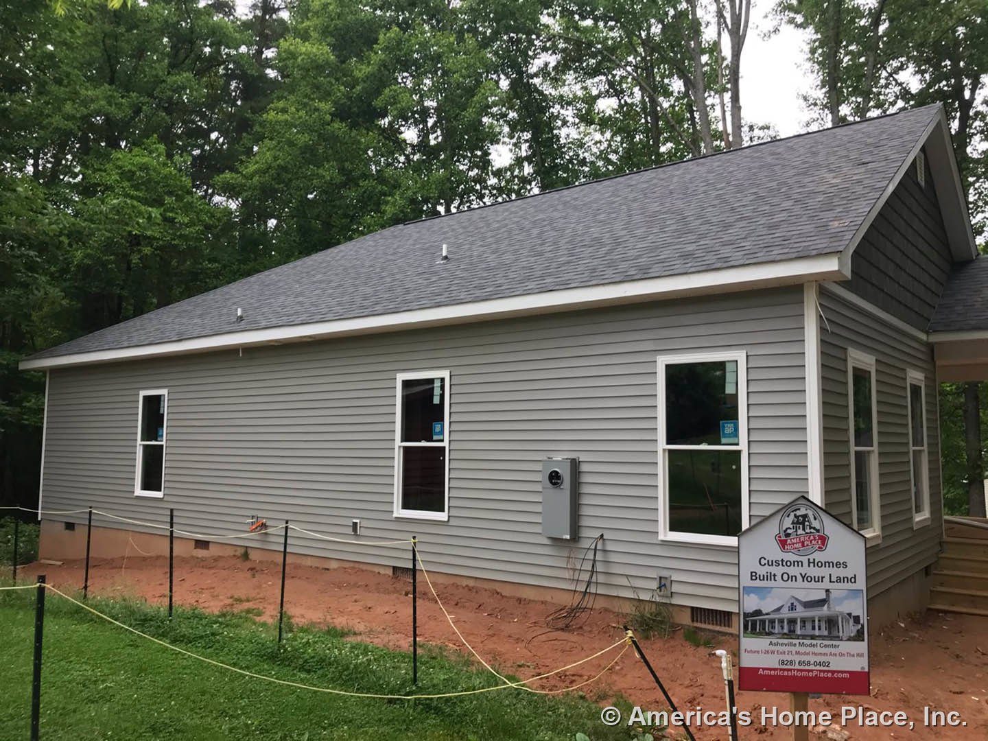 Grey siding home with white trim, large front window, fenced yard with green grass and yellow rope, real estate sign displayed near entrance.