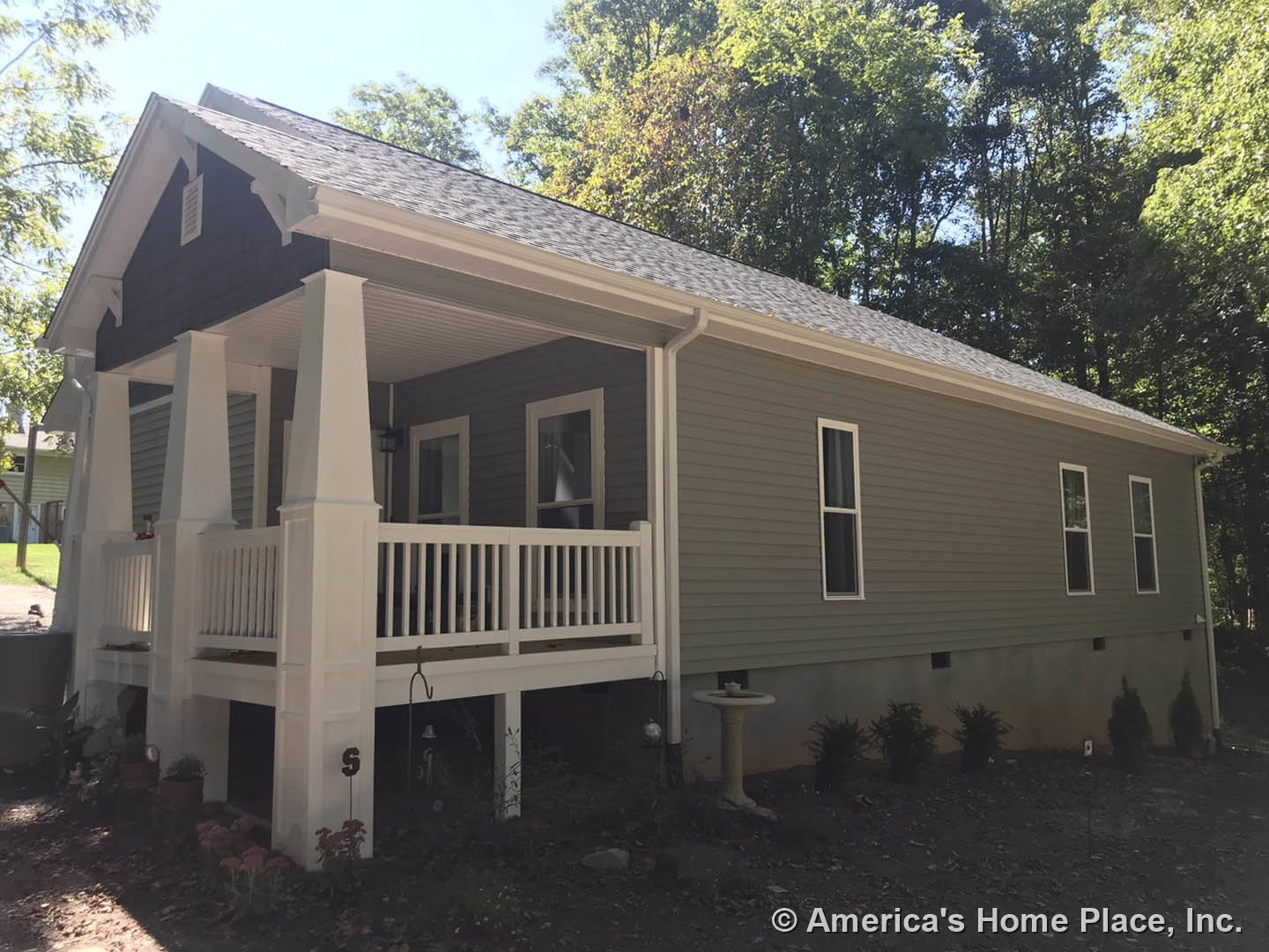 Two-story cottage with light siding, covered front porch, white-framed windows, potted plants, and mature trees in the yard
