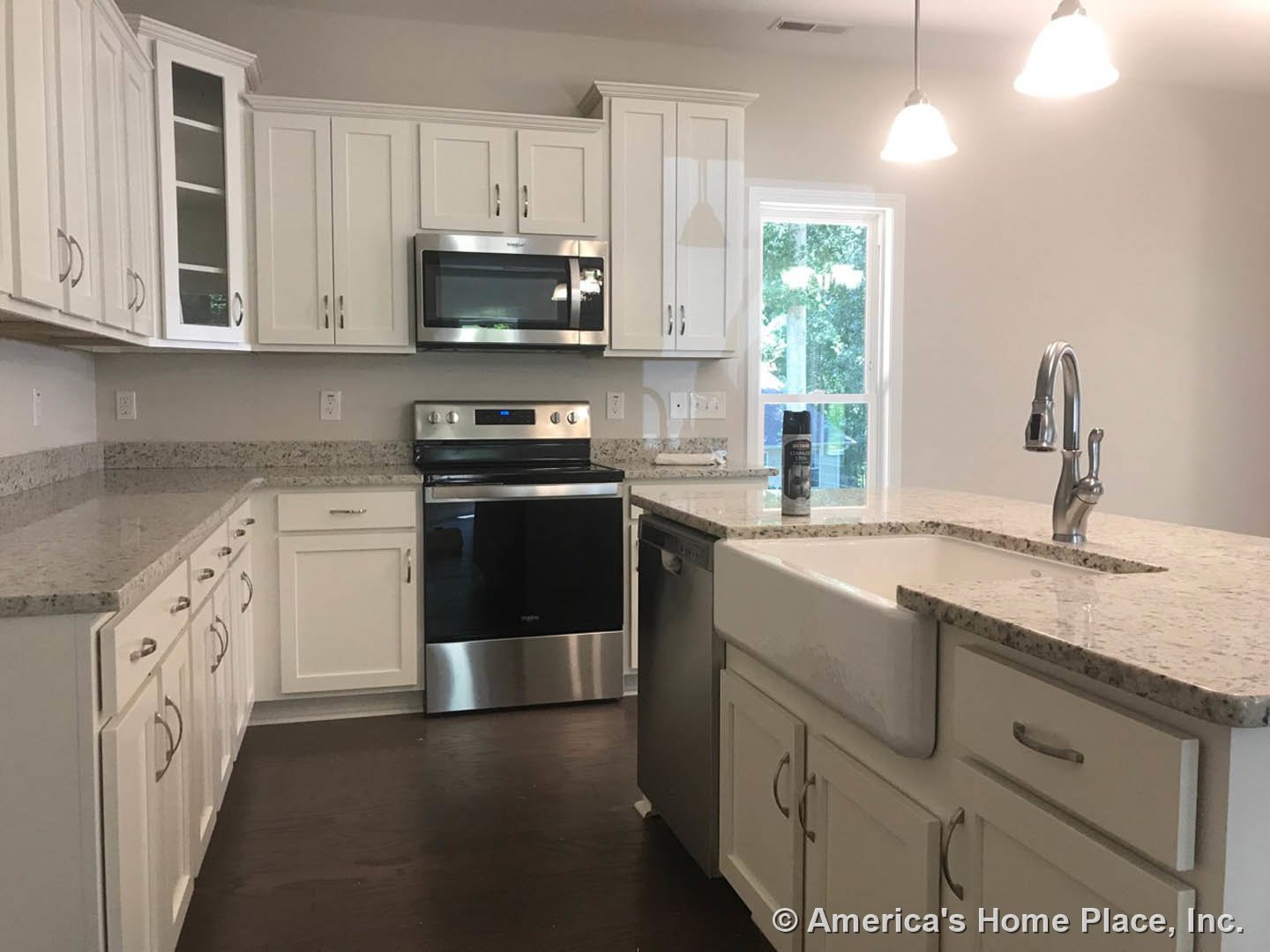 White kitchen cabinets with granite countertops, open microwave door, black and silver oven, chrome faucet, window overlooking trees, white cabinet with metal handle