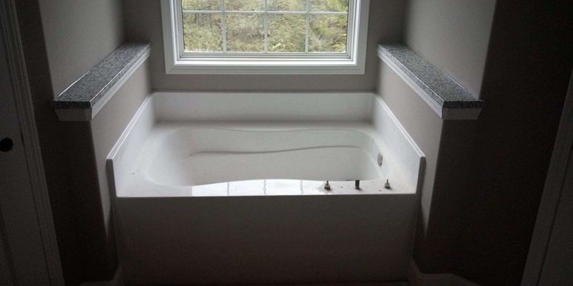 Freestanding white bathtub beside a large window, white toilet and tiled walls in modern bathroom