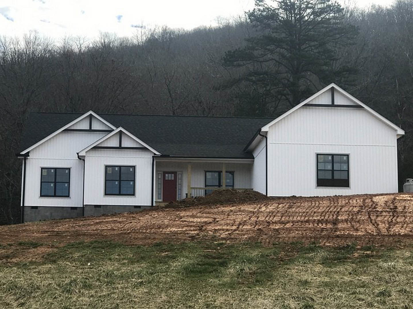 White house with black roof, black-framed windows, and square panes, set on grassy lawn with hill and trees in the background