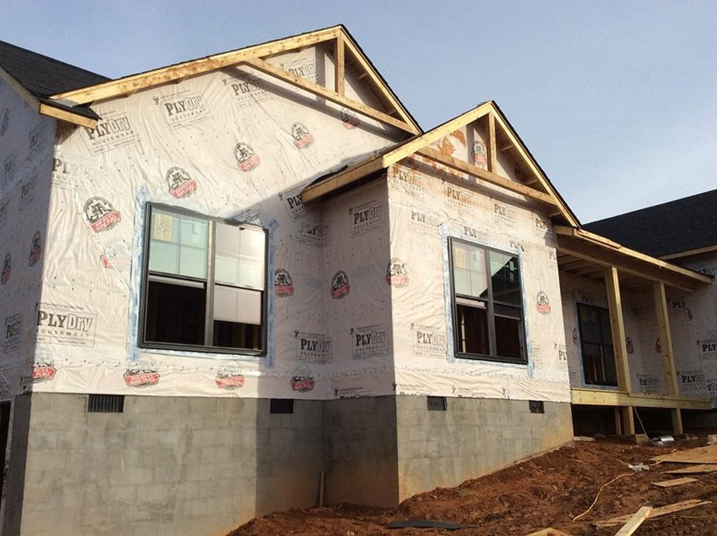 Framed house under construction with completed roof, exposed plywood walls, and dirt yard foreground