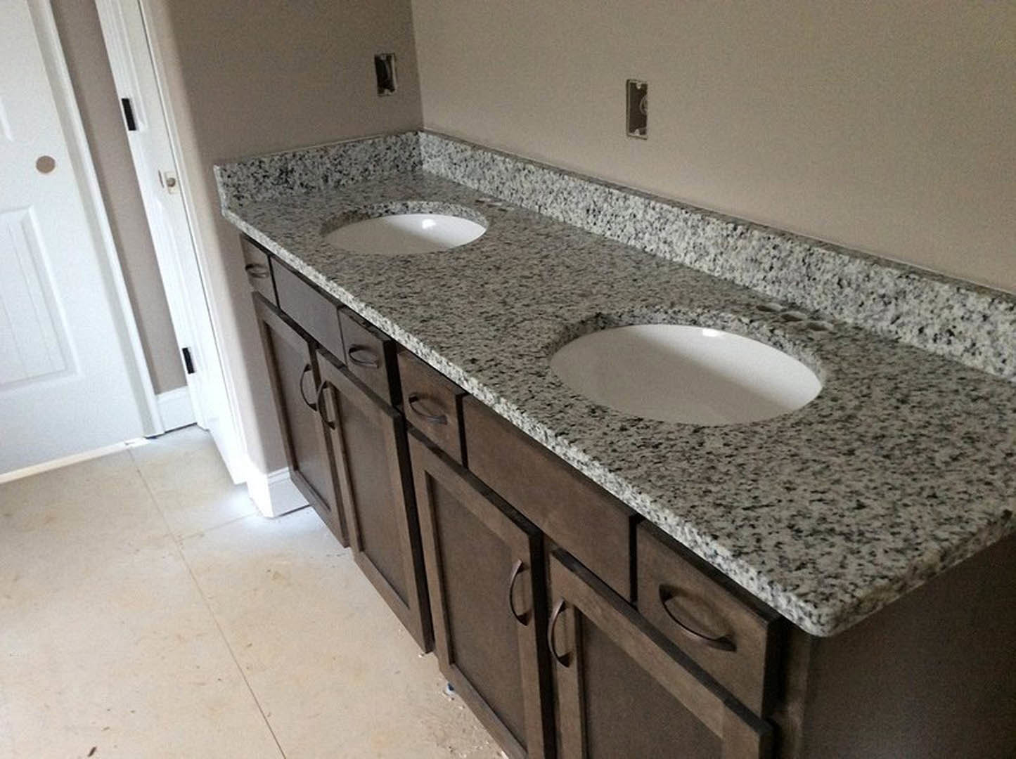 Bathroom with granite countertop, undermount white sink, chrome faucet, white tile flooring, and light wood cabinetry
