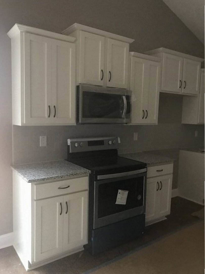 White shaker cabinets, stainless steel stove, built-in microwave, paper resting on oven door, light quartz countertops, tile backsplash, wood flooring
