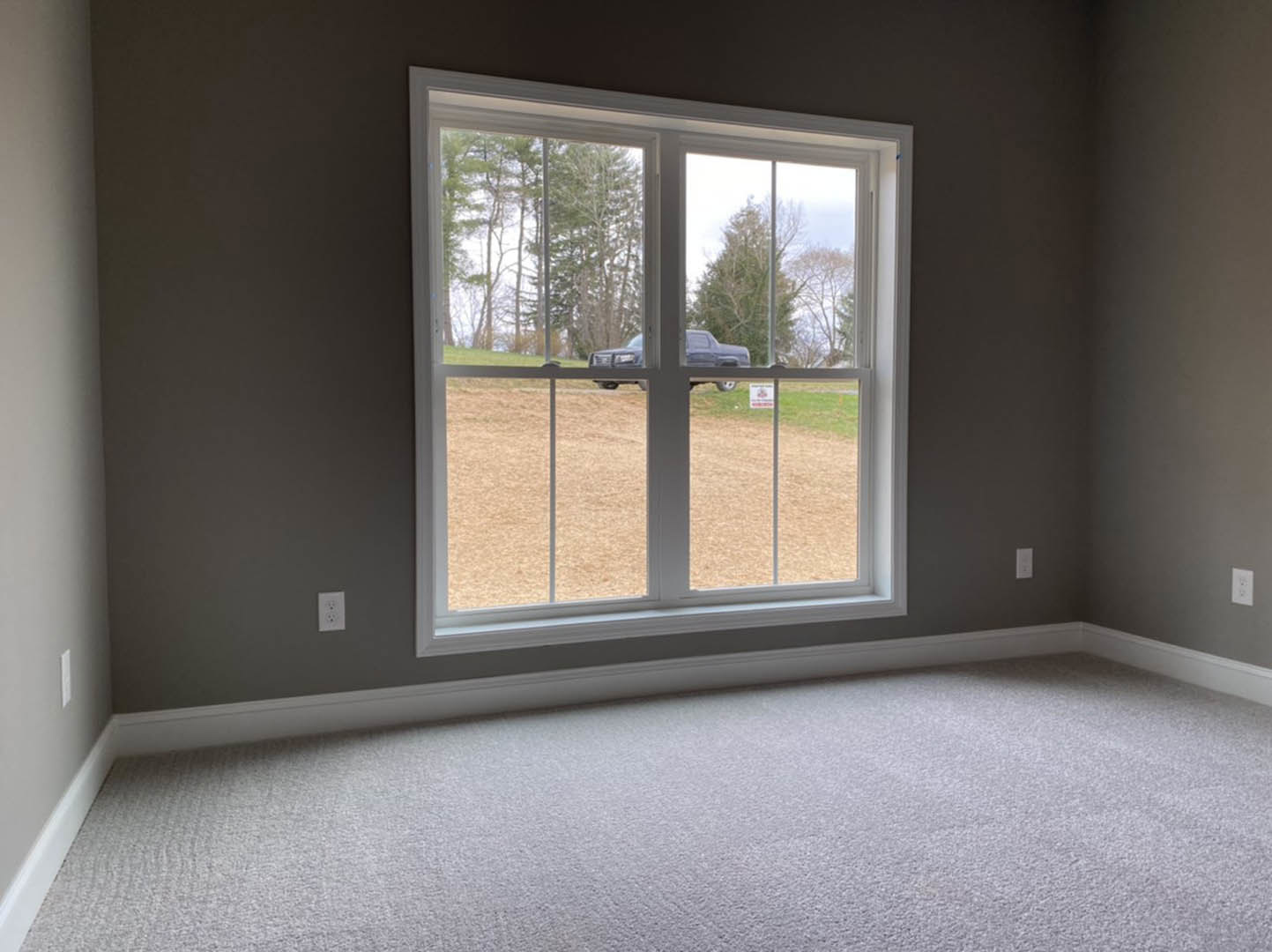 Neutral-toned carpeted room with white walls, large window, and parked vehicle visible outside