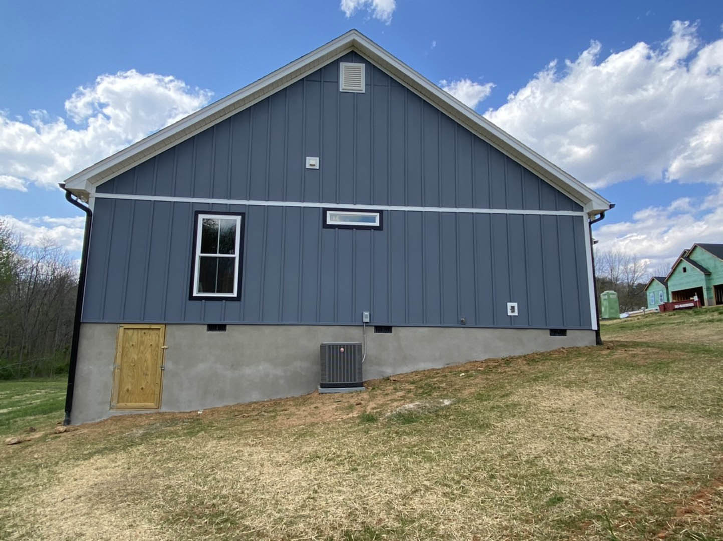 Blue exterior wall with wooden door and window, surrounded by grass under a partly cloudy sky