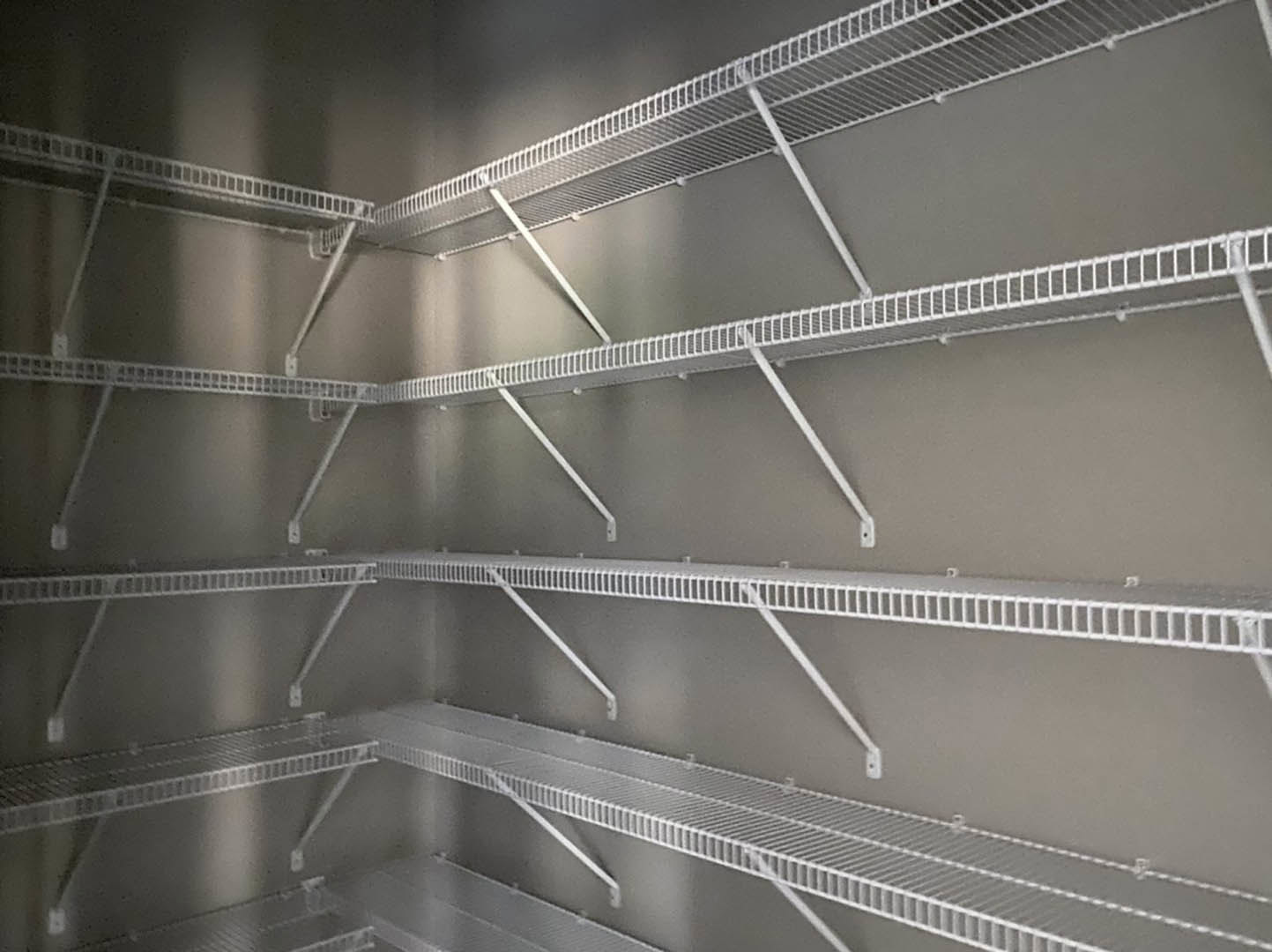 Empty closet with white metal shelves and rods against a gray wall