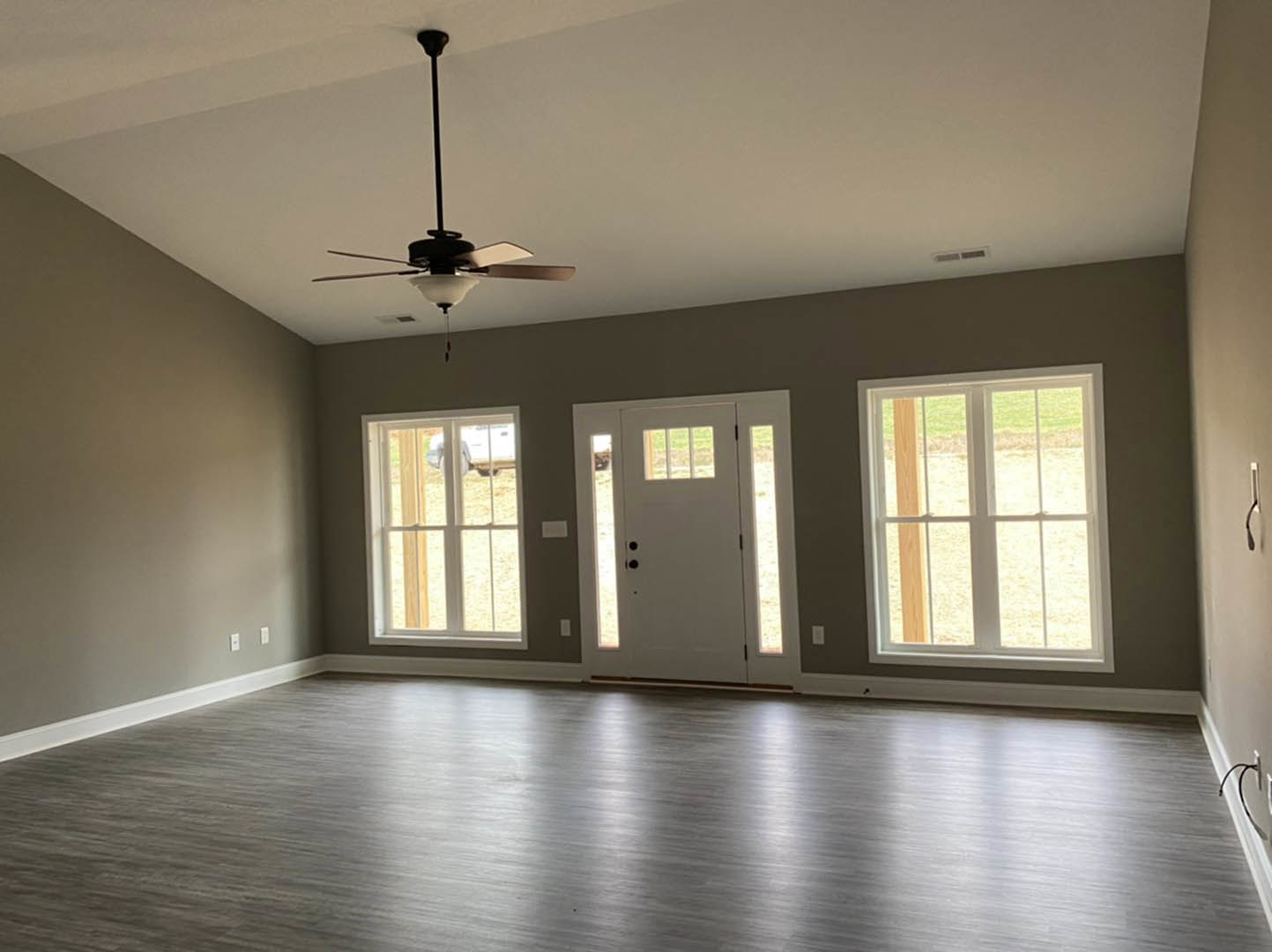 Ceiling fan with light fixture above wood floor, white-framed windows, and white door with glass panels in a bright room with plaster walls and ceiling
