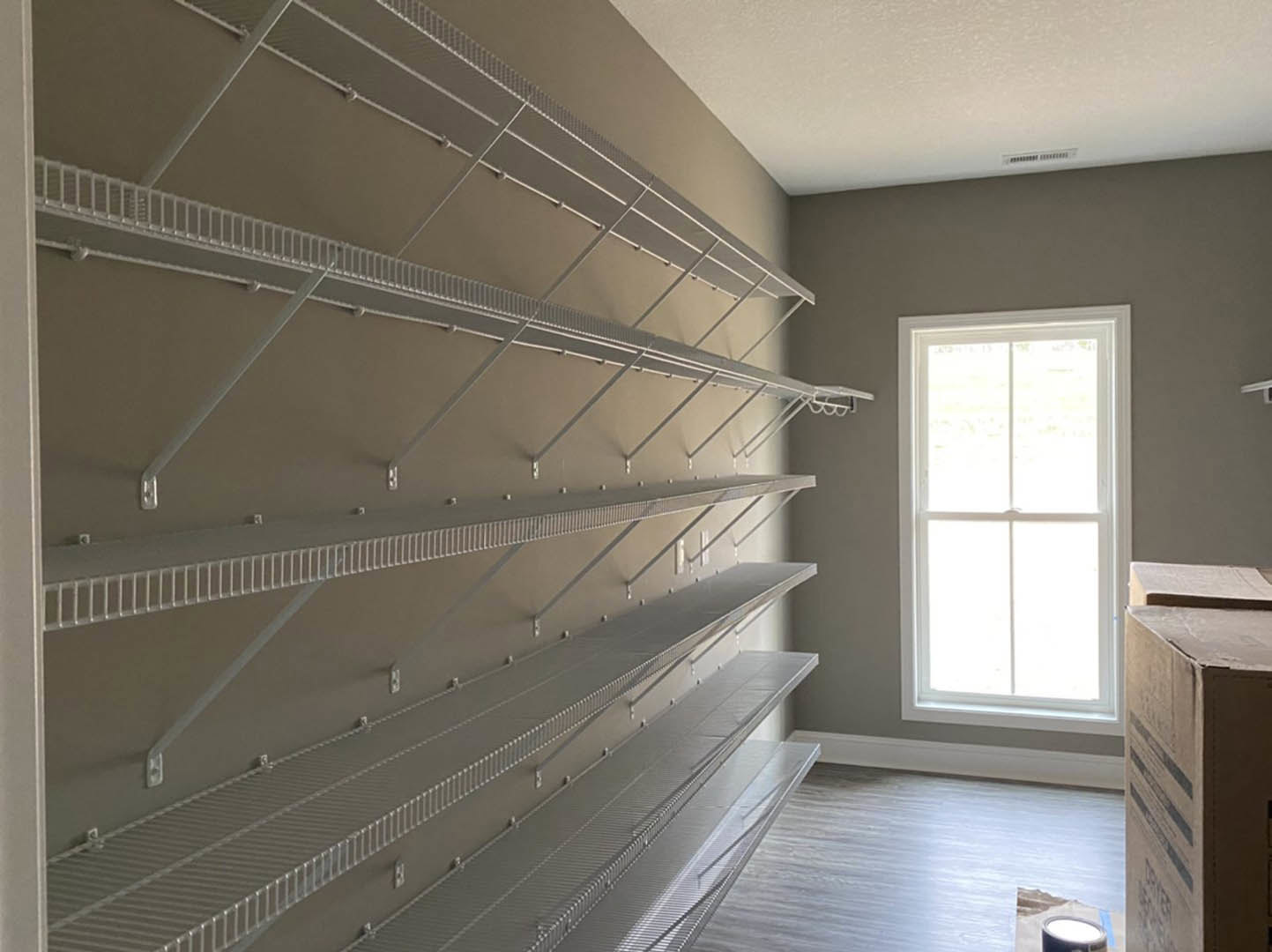 Built-in white shelves on a plaster wall beside a window, white floor and door visible in a minimalist room