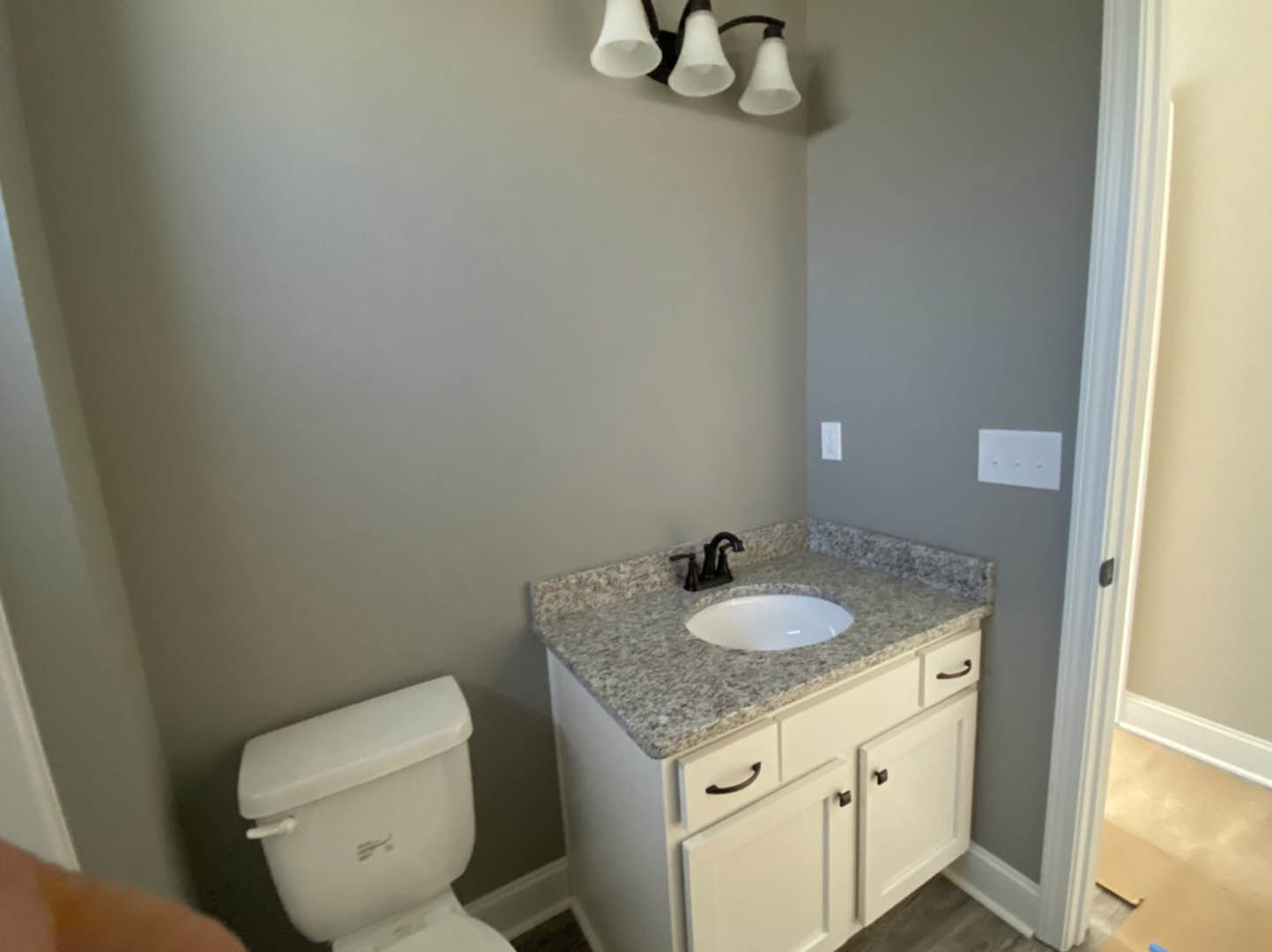 White porcelain sink with chrome faucet set in a light wood vanity, adjacent to a modern toilet, gray tile flooring, and neutral wall tiles
