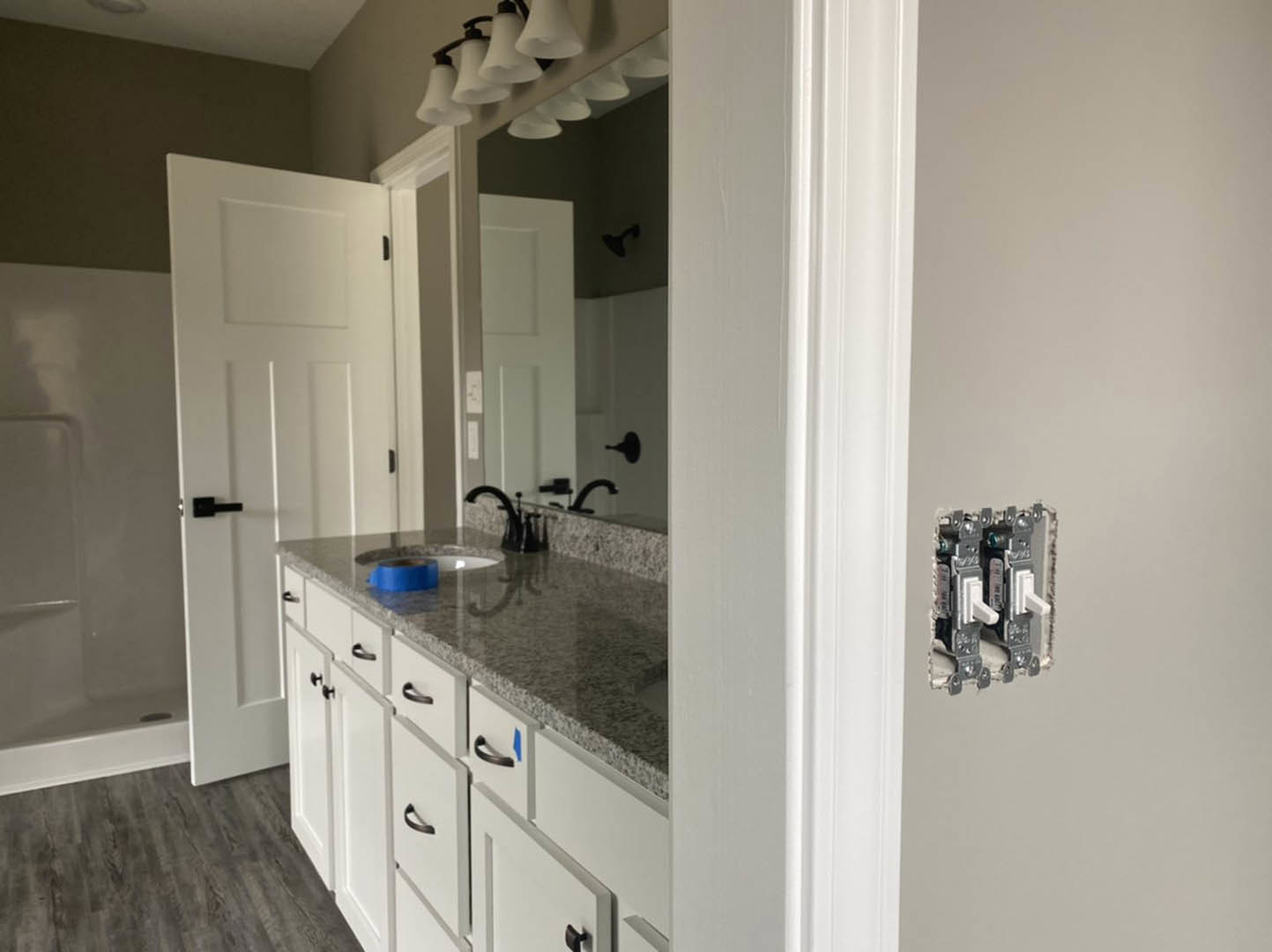 Modern bathroom with white tile walls, rectangular mirror above a sleek sink, black faucet, white door with black handle, metal-framed wall lights, blue cup with brown rim on