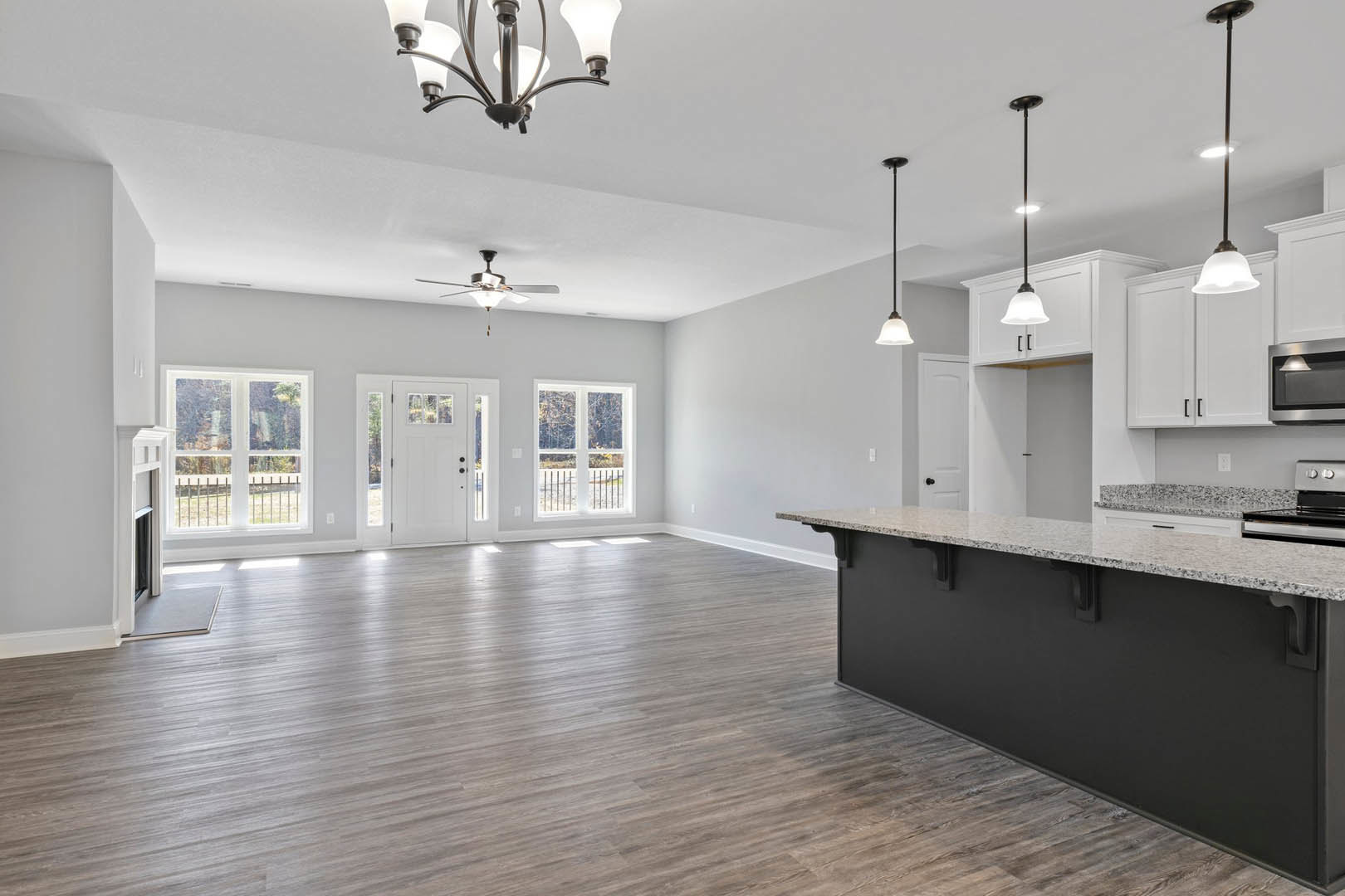 Open-concept kitchen with expansive island, white cabinetry, stone countertops, hardwood flooring, modern chandelier, stainless steel appliances, and large windows with railing