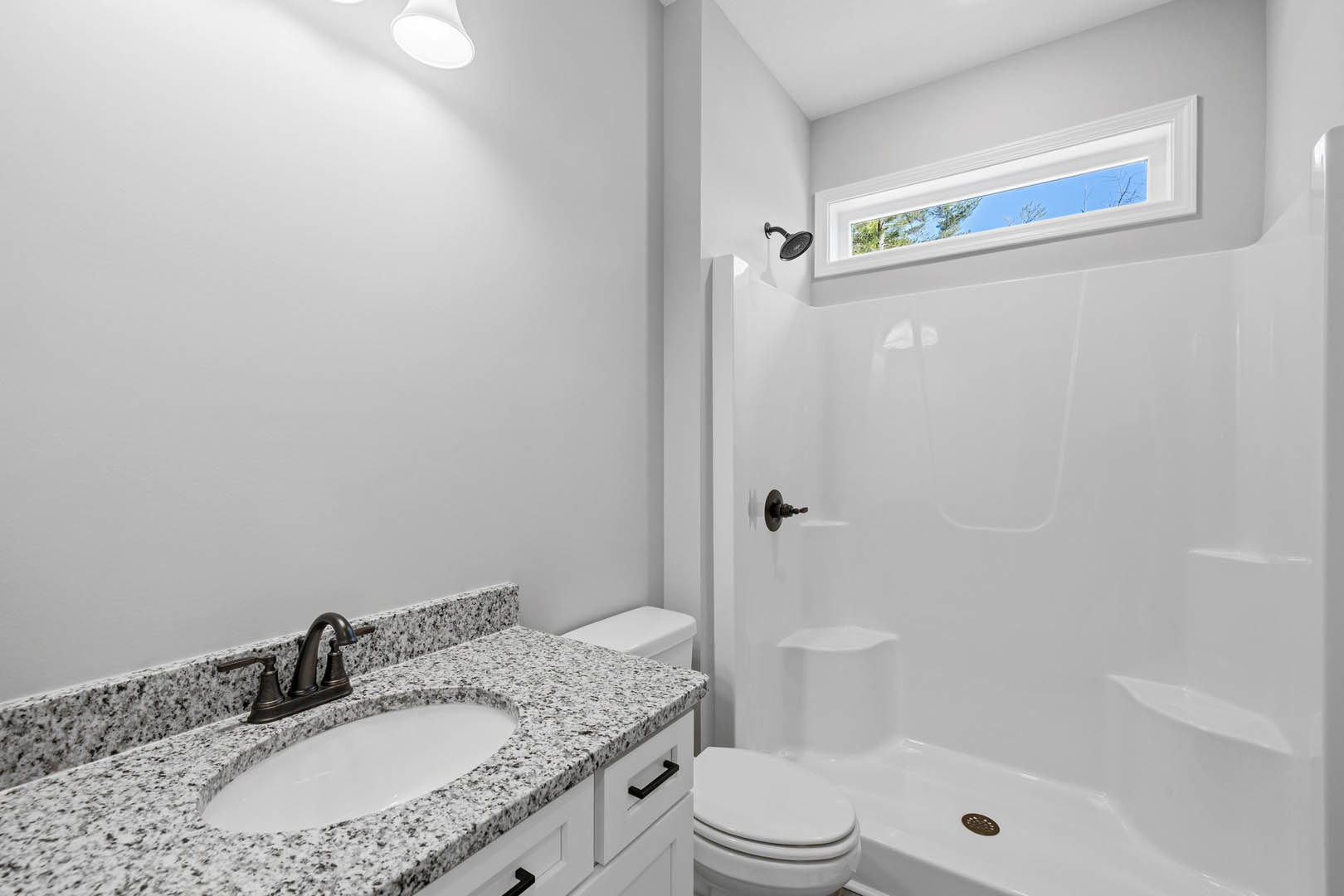Modern bathroom featuring a white sink with chrome faucet, glass-enclosed shower, tiled walls, toilet with lid open, and a window showing blue sky.